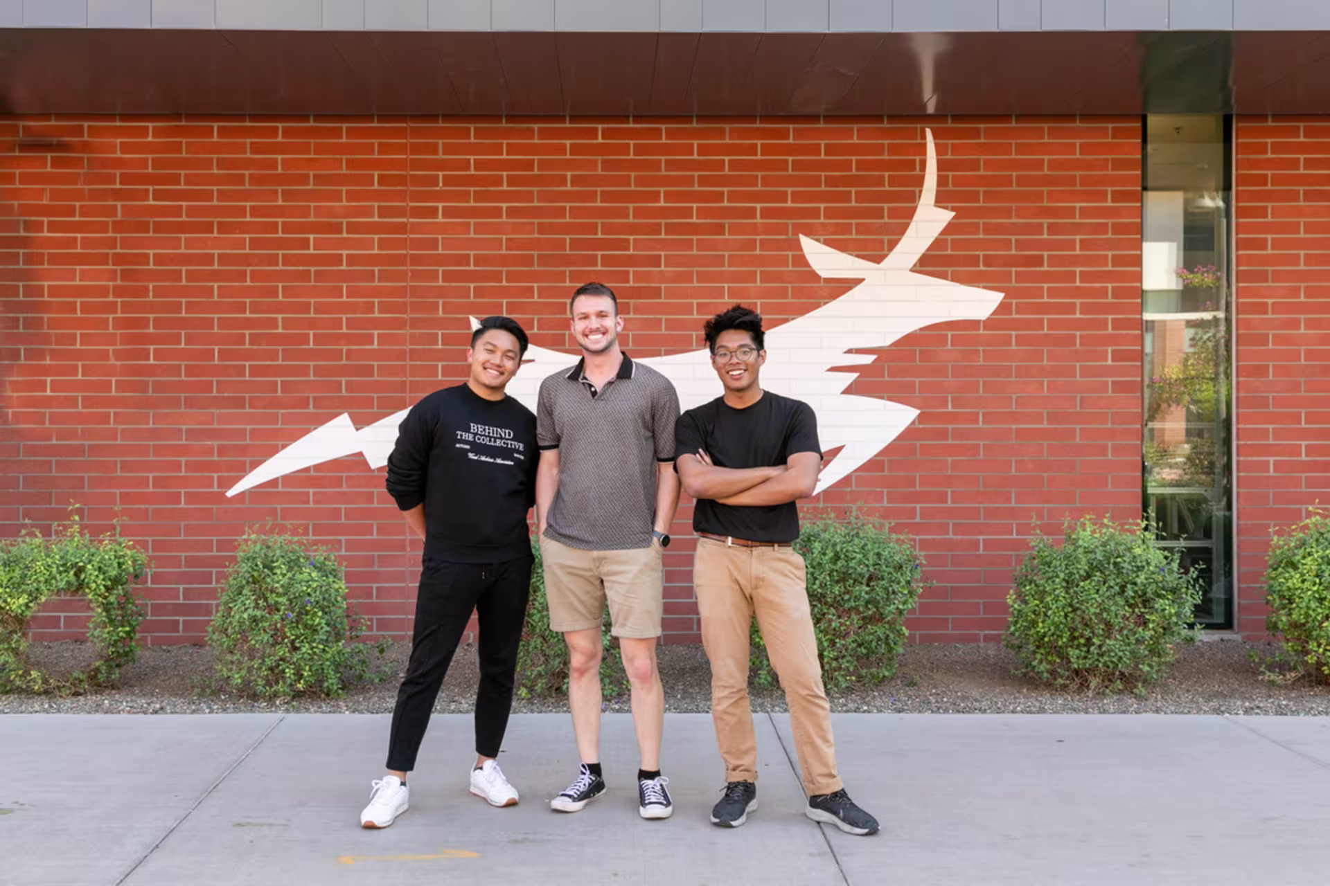 Trio of gcu male students in front of brick building painted with GCU lope.