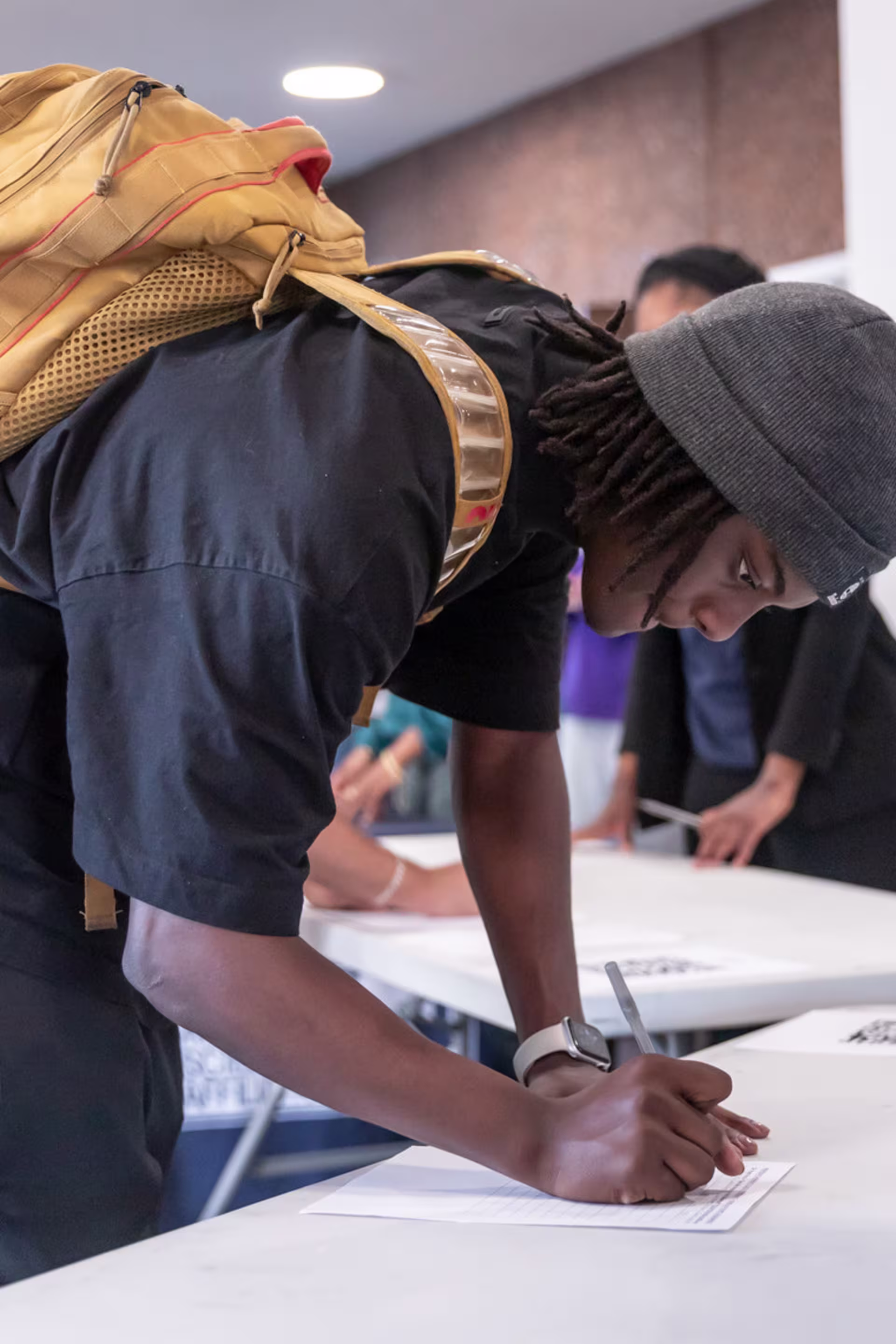 black male prospective student fills out paper form by hand on white table