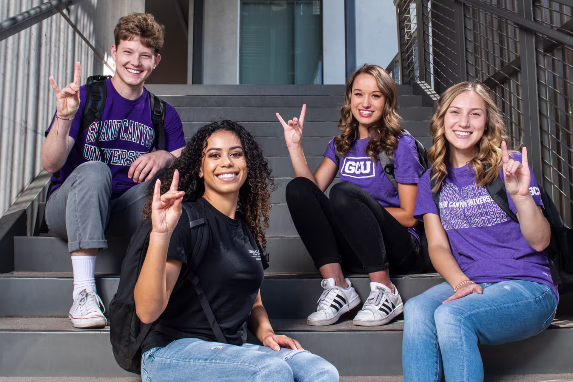 A group of honors college students sitting on steps outside giving the Lopes Up hand symbol.
