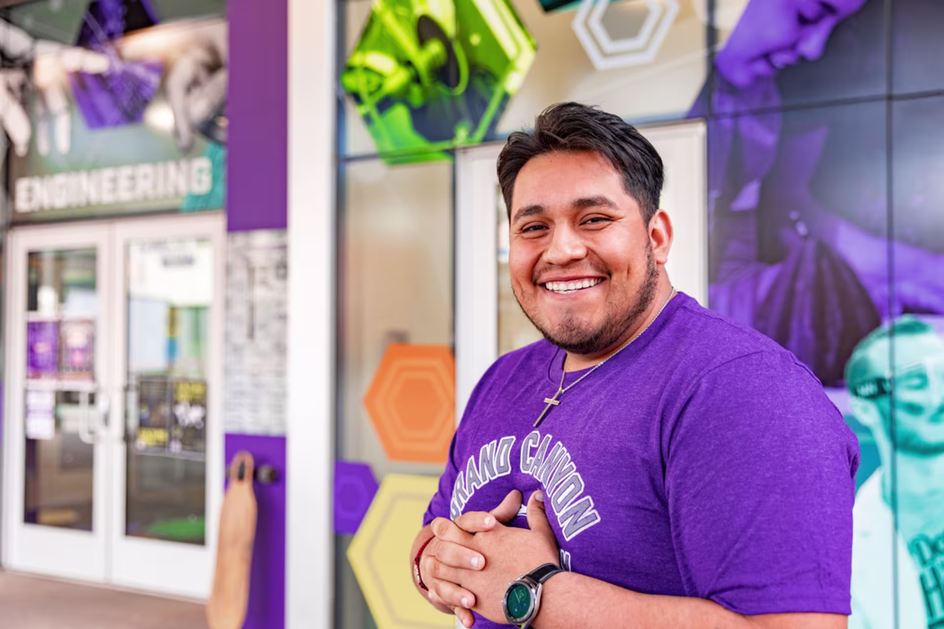 hispanic male student in purple gcu shirt stands near engineering lab door