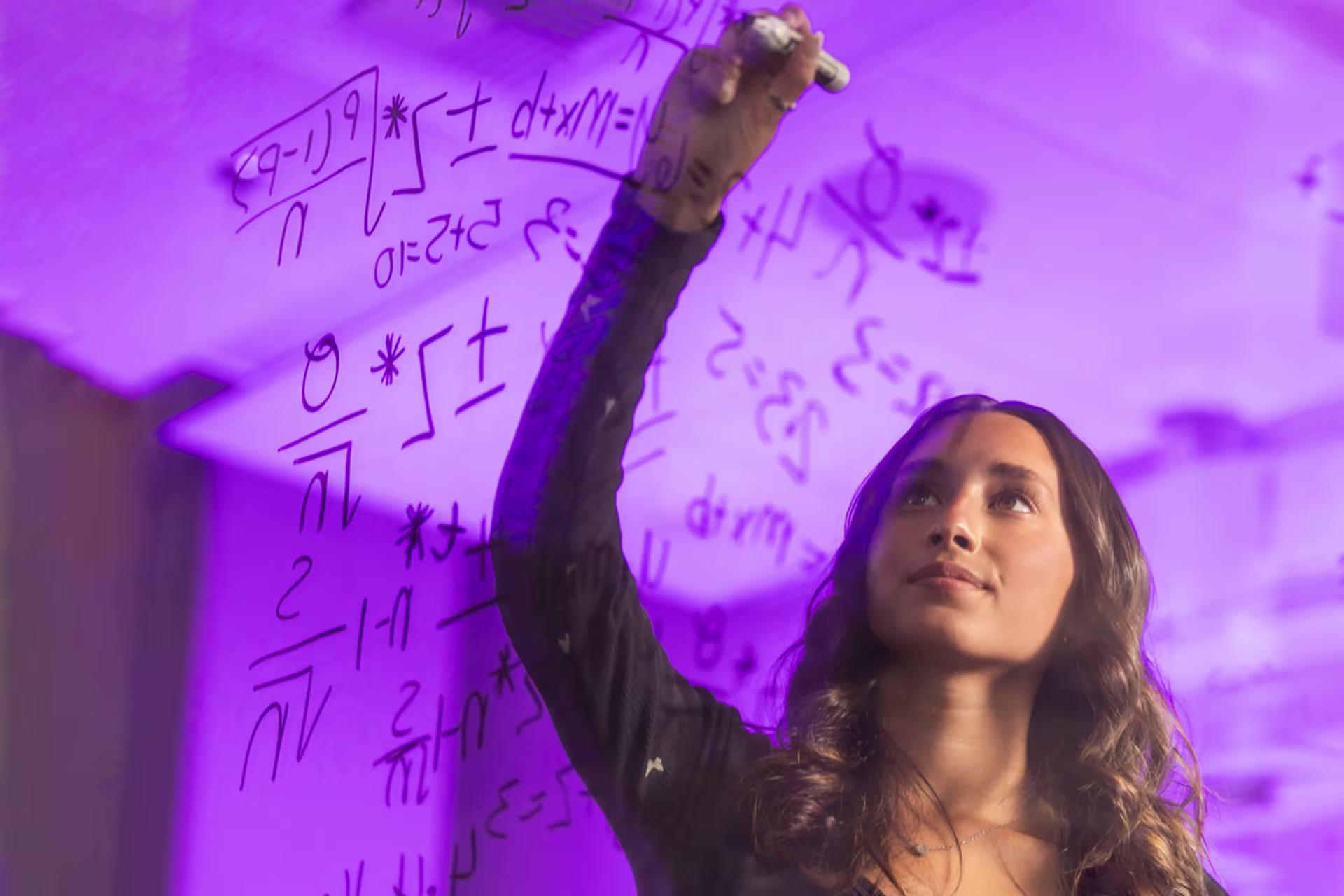 female student writes equations on a glass board for machine learning