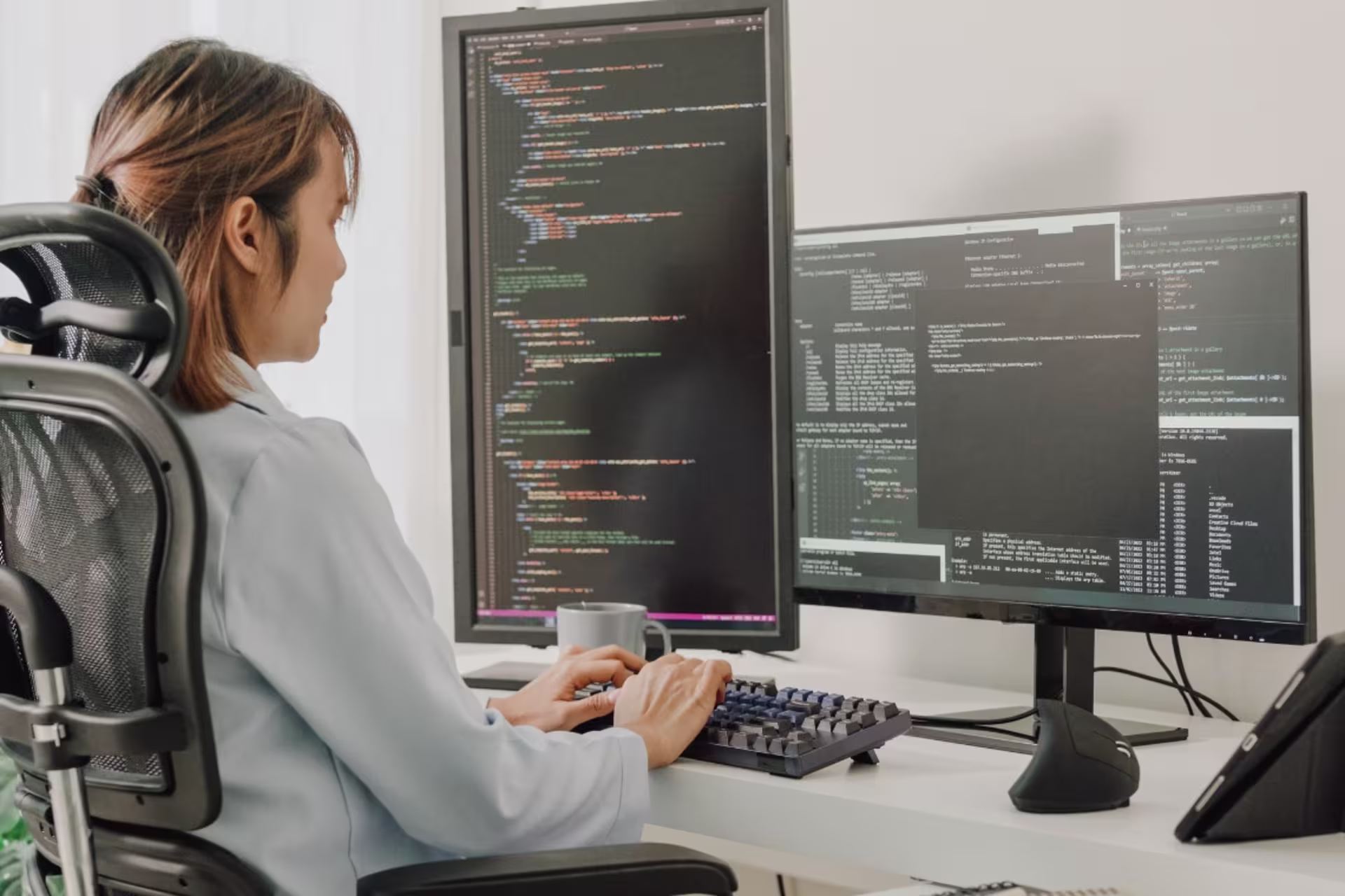 Java developer sitting at a table and working on two computers with code on them
