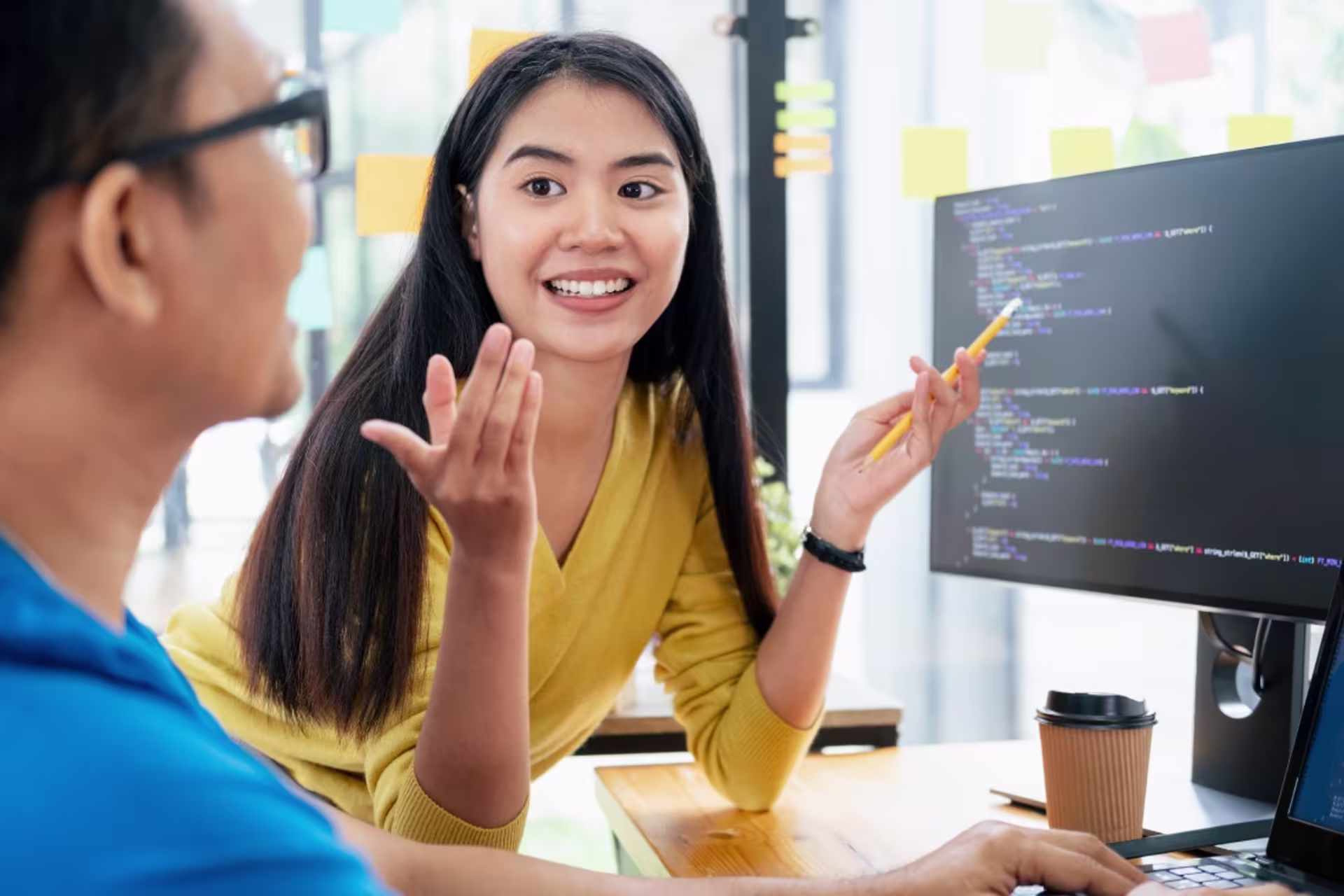 Java developer with a coworker at a desk while discussing code on the computer screen