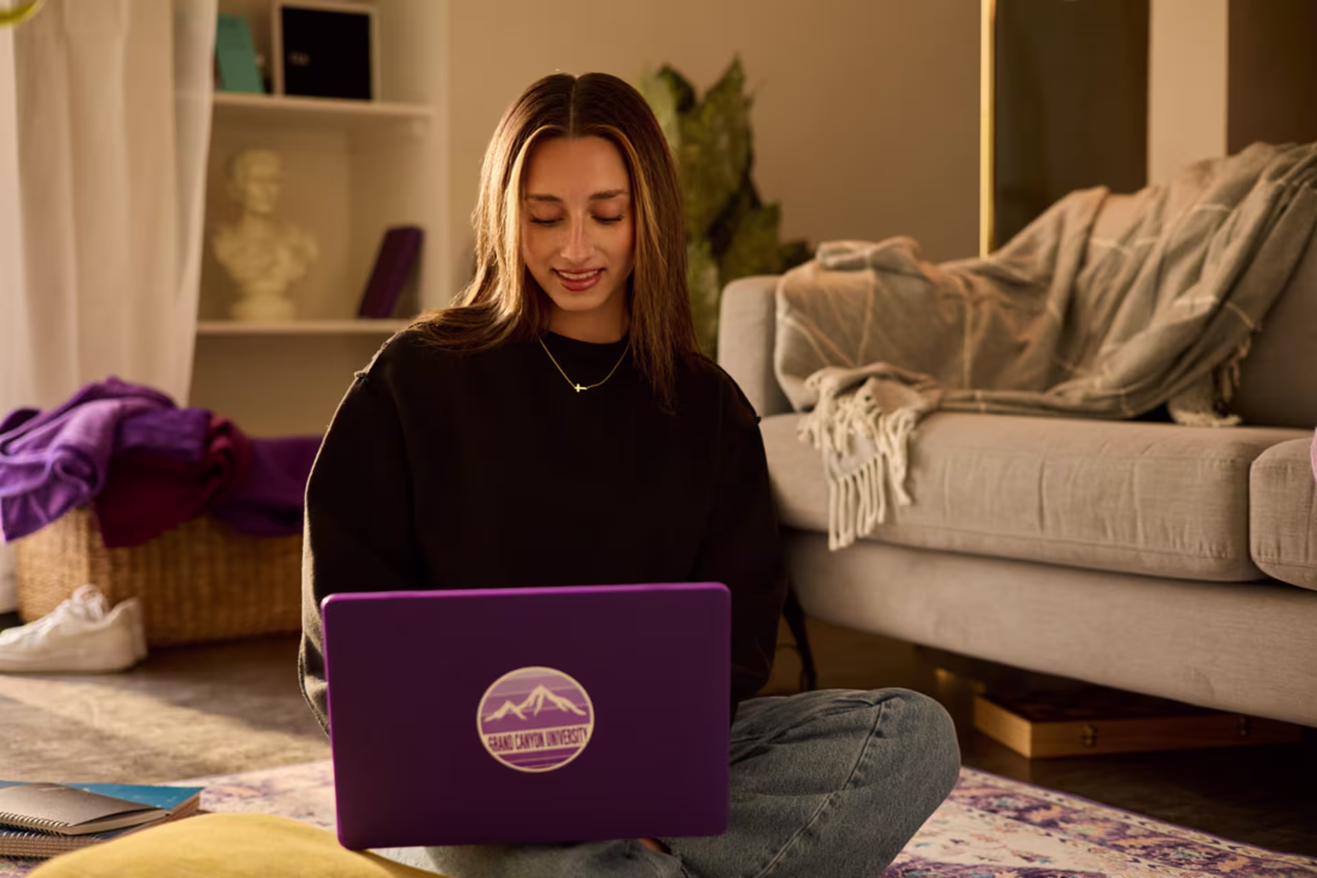 brunette female student uses laptop sitting on floor with notebooks close by