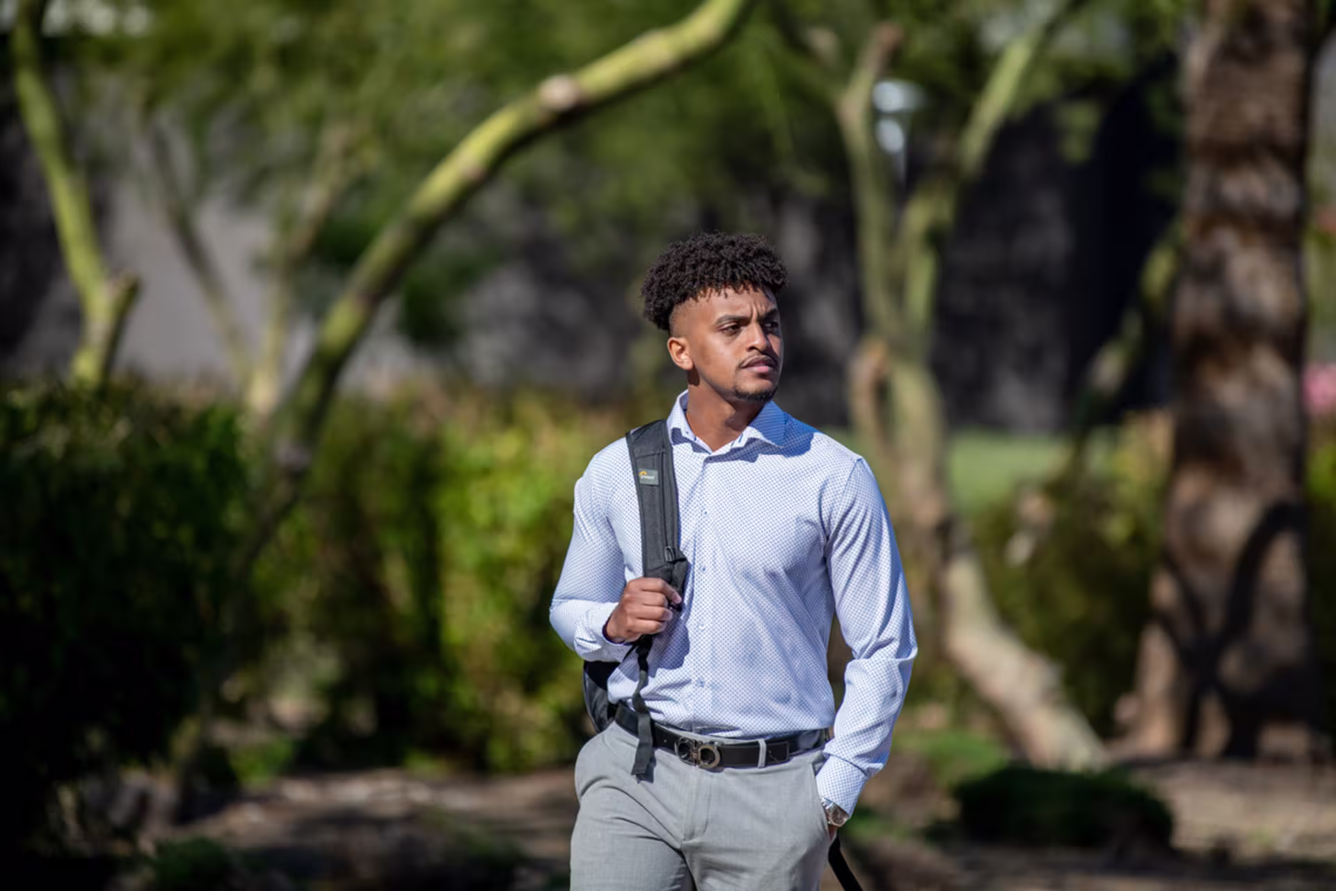 black student nicely dressed with backpack on one shoulder walks on campus