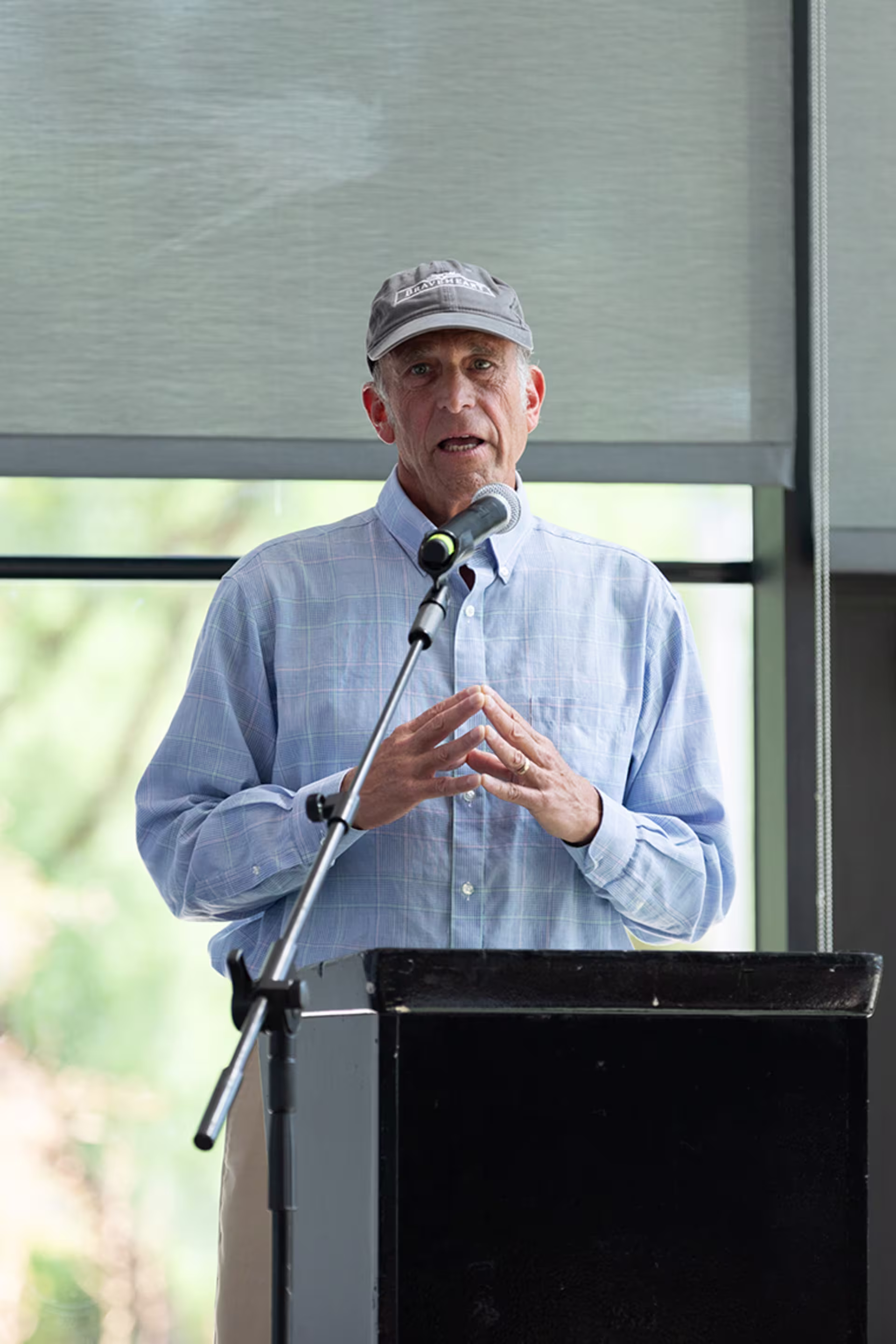 Older male finance emphasis speaker in light blue button-down talking to crowd
