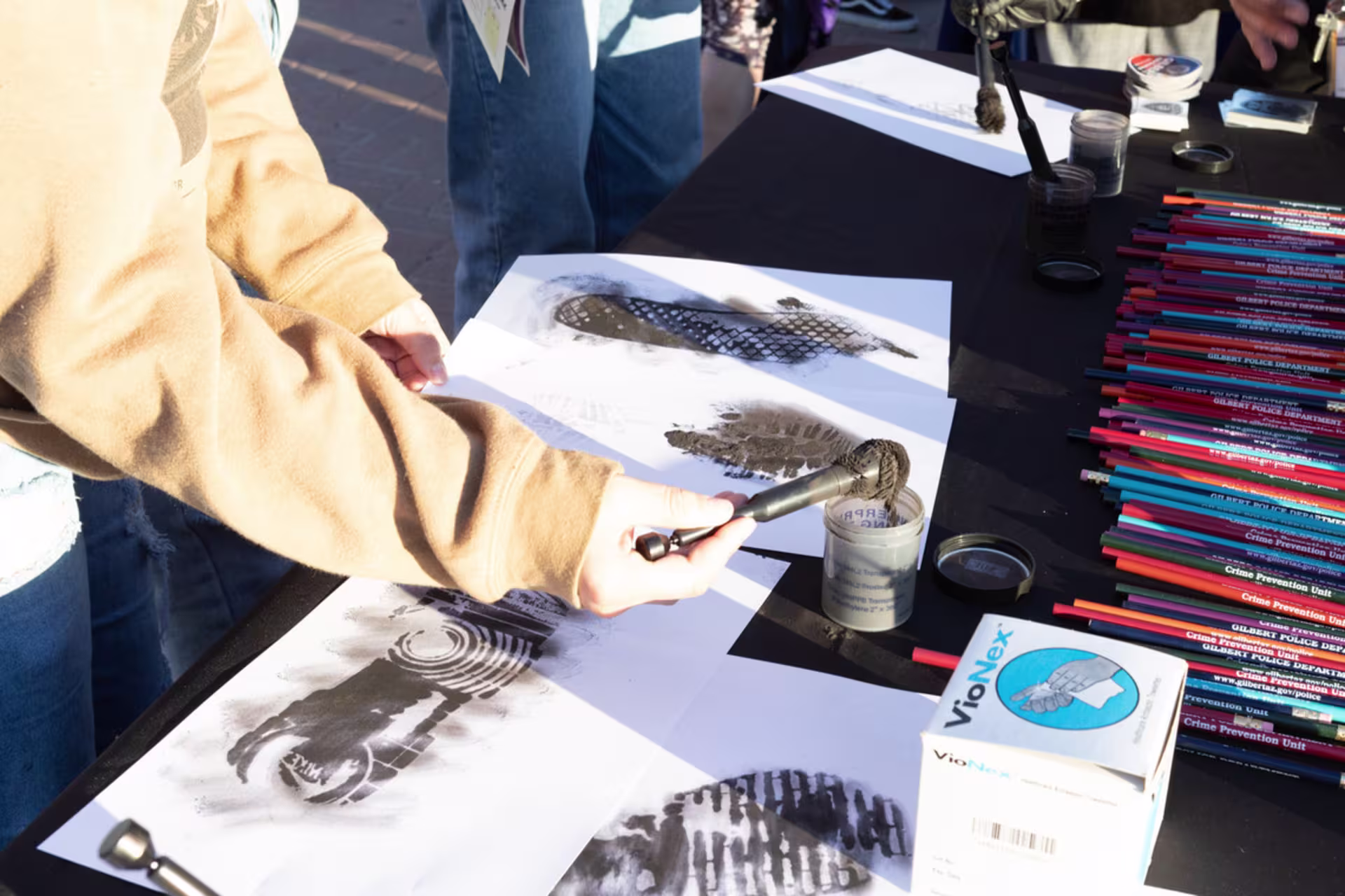students make shoe impressions with paper and gray powder at forensic science day booth