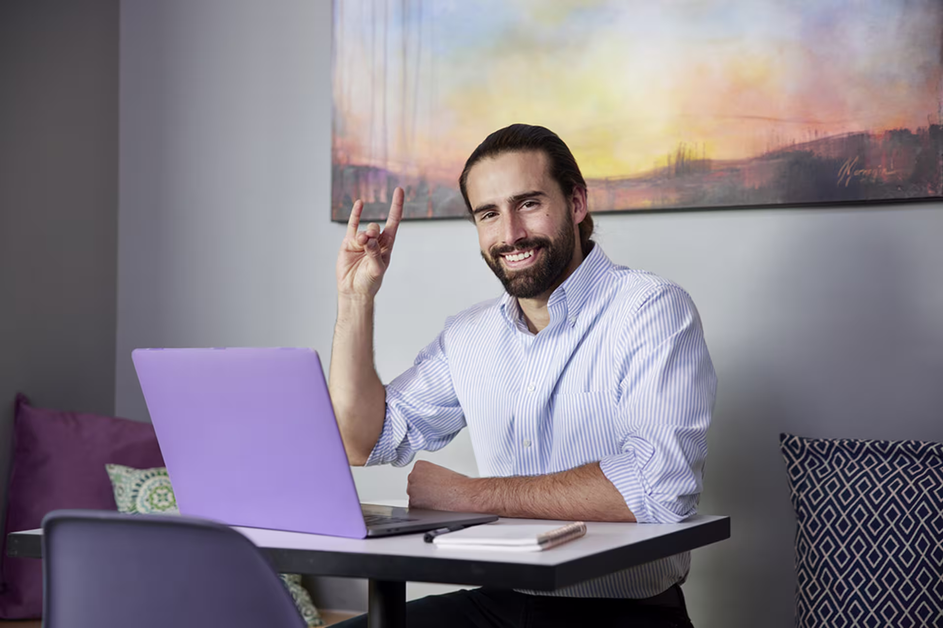 Male student studying on laptop in coffee shop and throwing up Lopes sign
