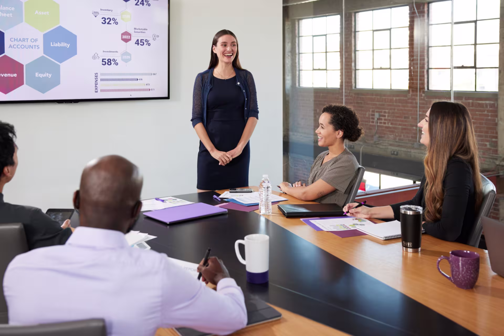 young woman stands to present marketing statistics at a business meeting