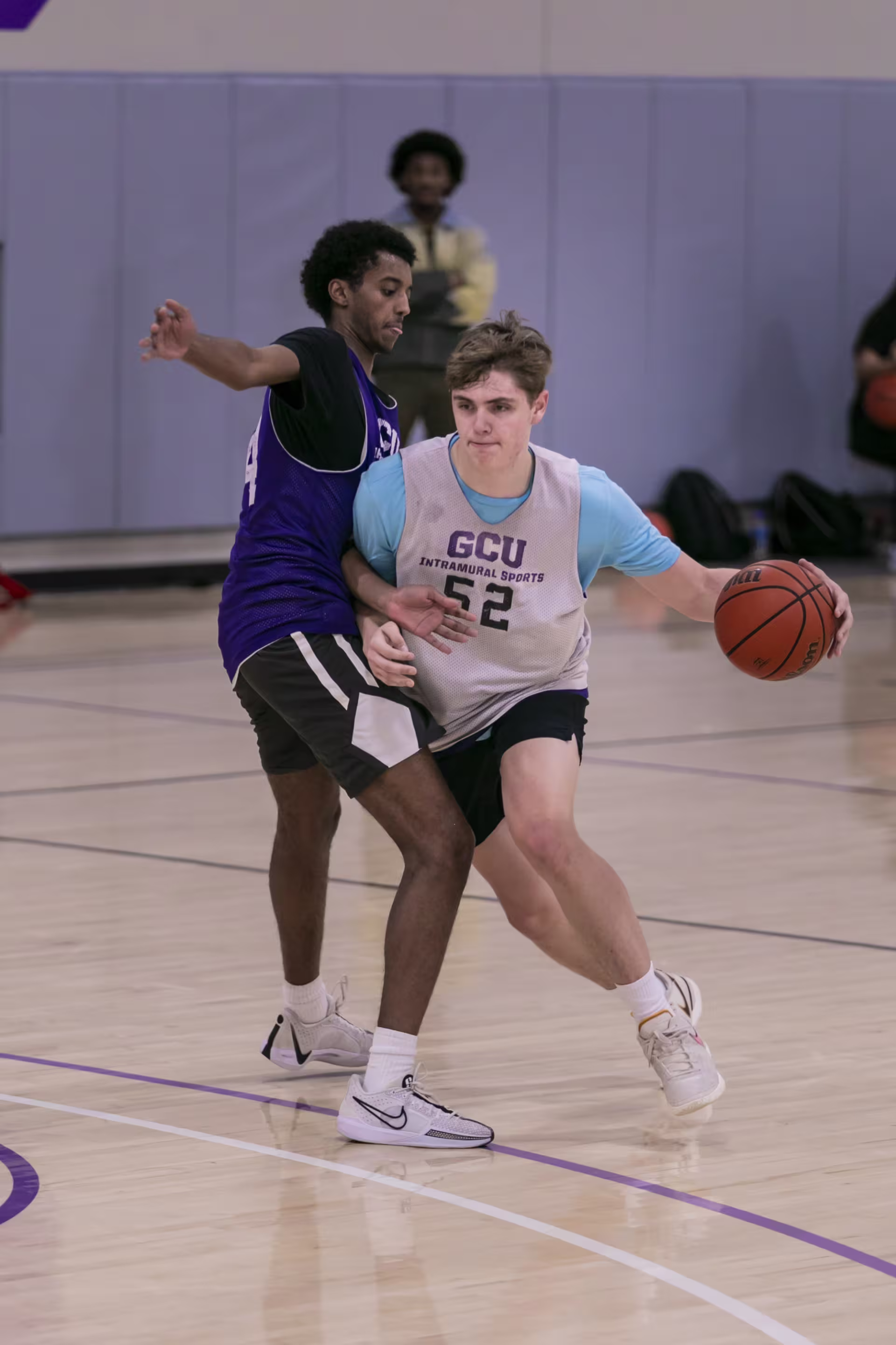male basketball player wearing a GCU intramural jersey dribbles the ball away from opponent trying to block his play