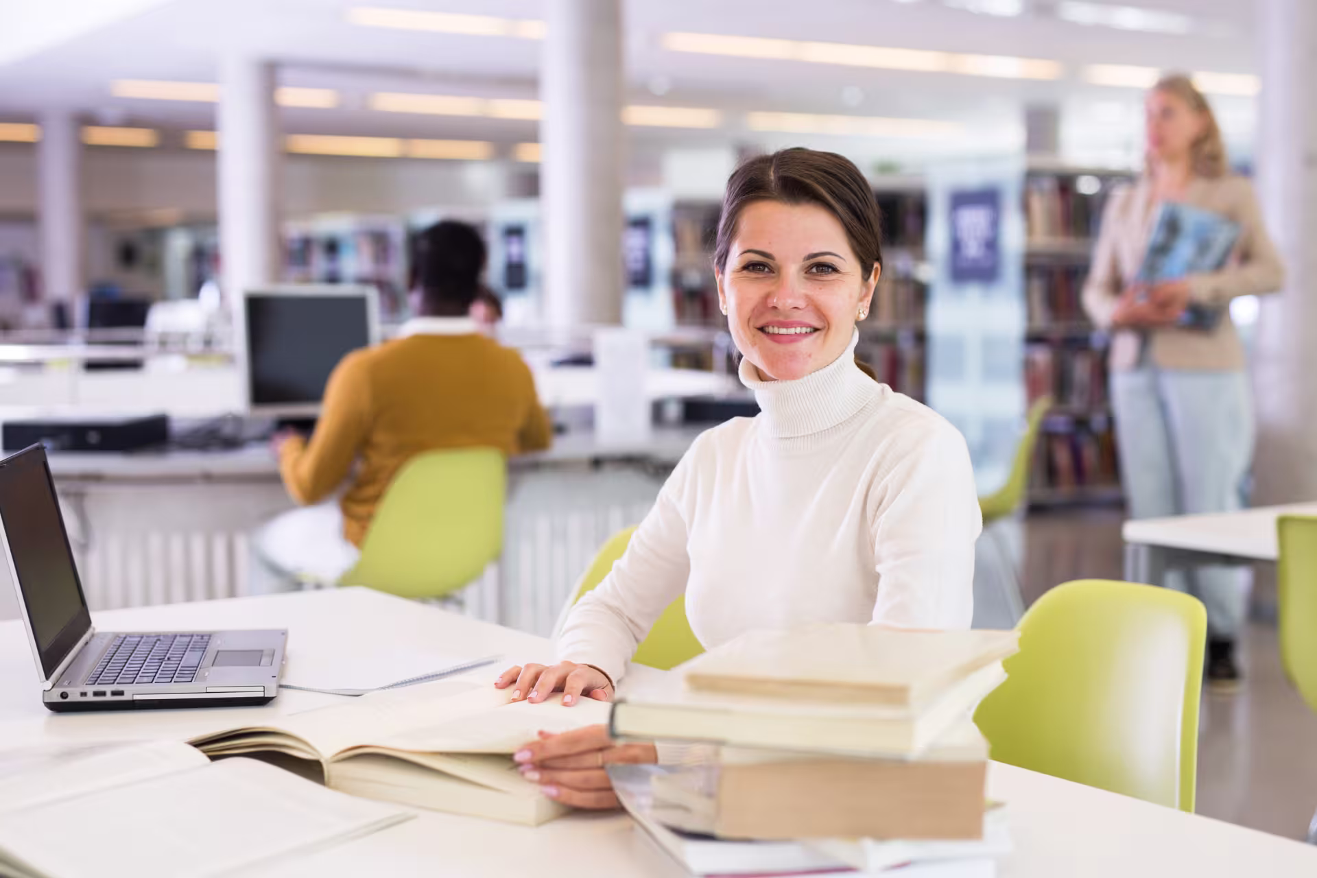 Woman sitting in college library while earning online degree on laptop.