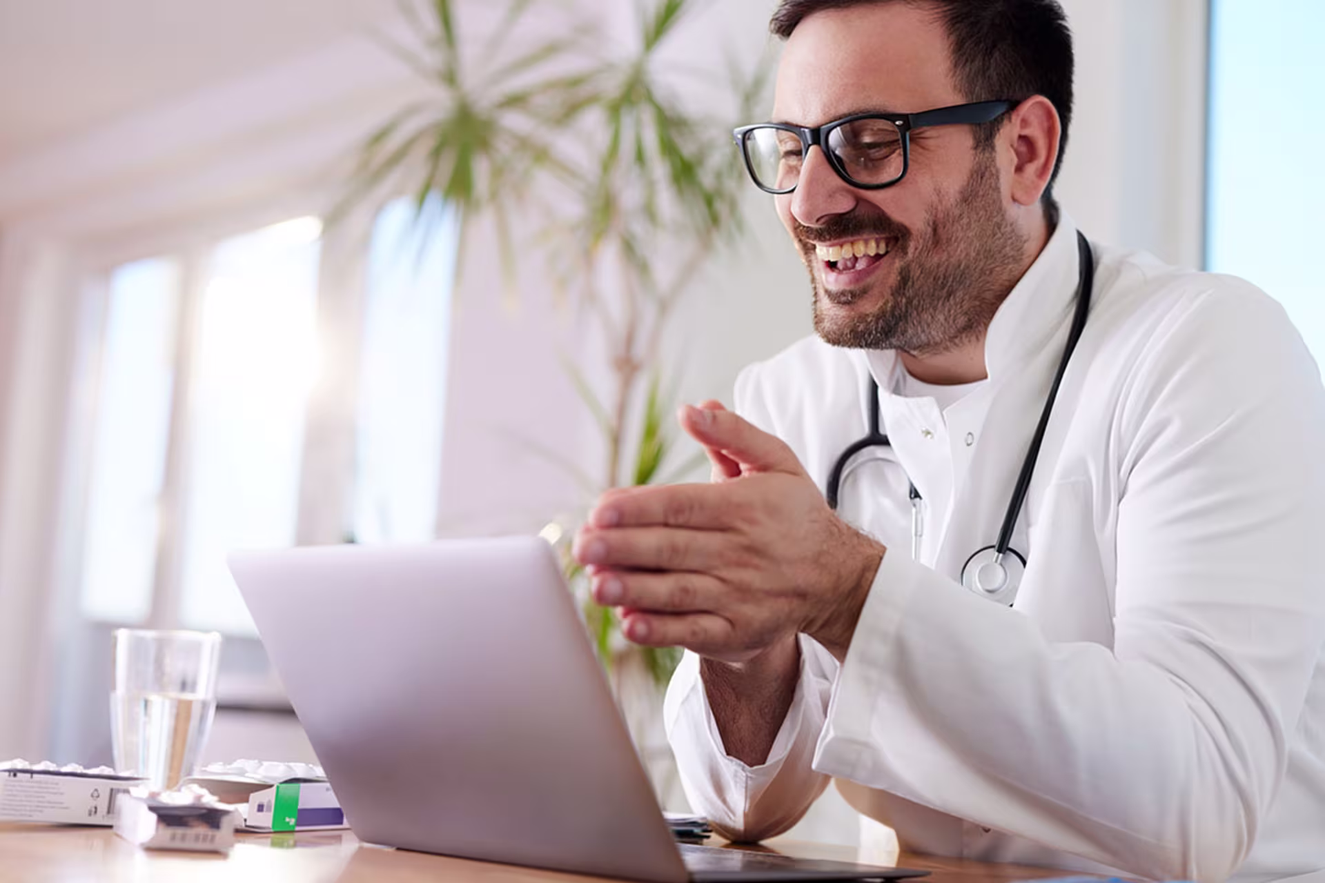 Male doctor smiling at laptop while hosting telemedicine call with patient