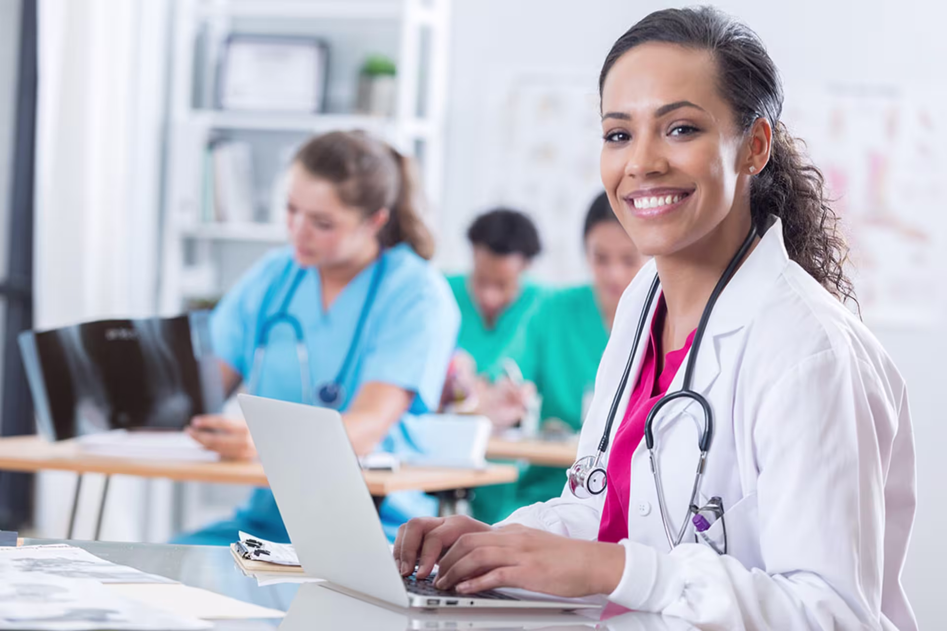 Female doctor in classroom smiling at camera while studying on laptop