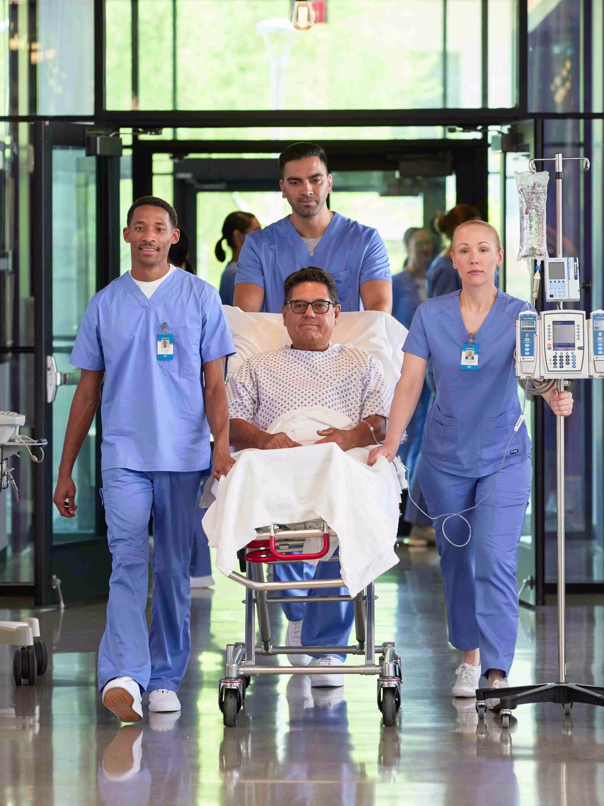 Group of male and female nurses in hospital hallway with patient on bed