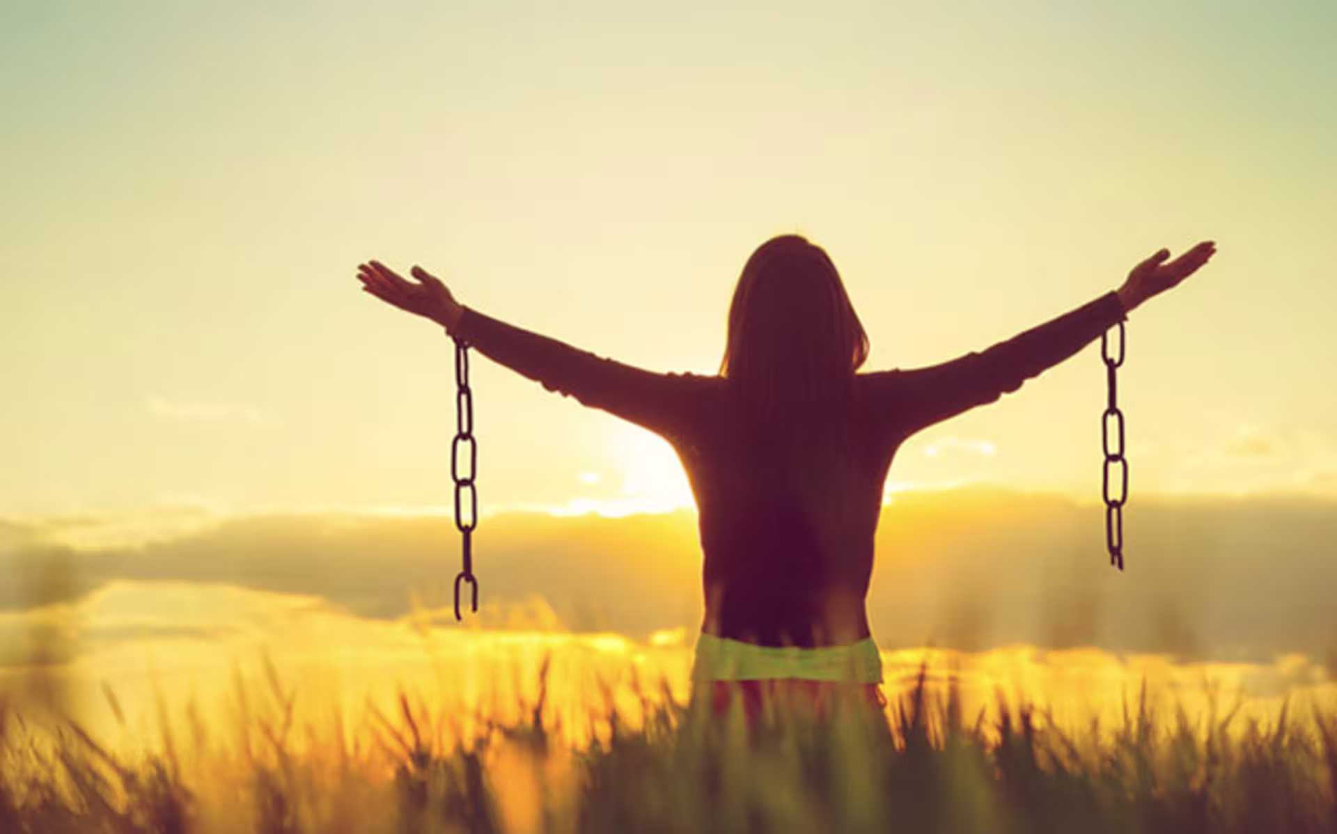 girl in field holding arms out with broken chains