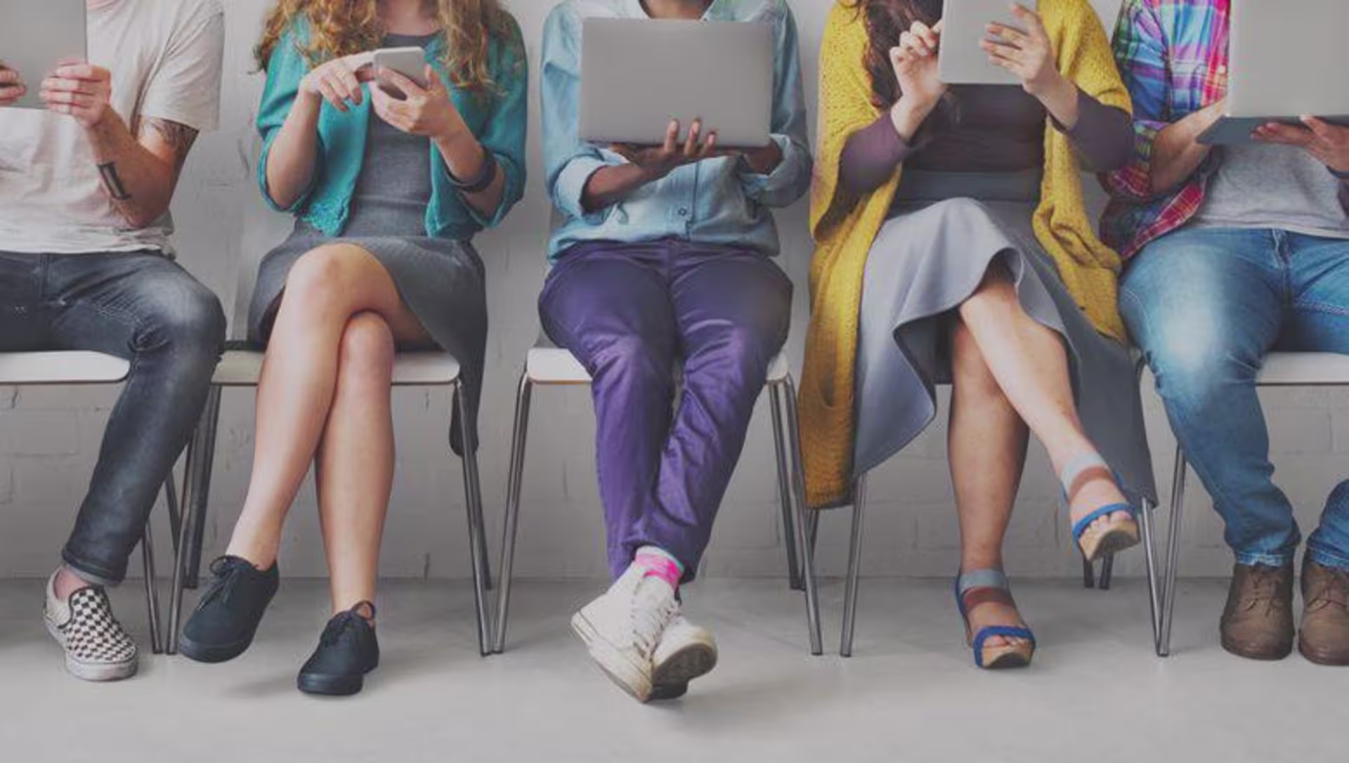 Front view of millennials sit in a row using phones and tablets