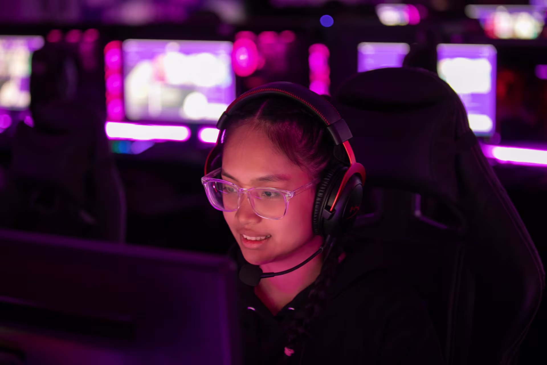 Female game development student wearing a headset in the GCU esports room with pink mood lighting