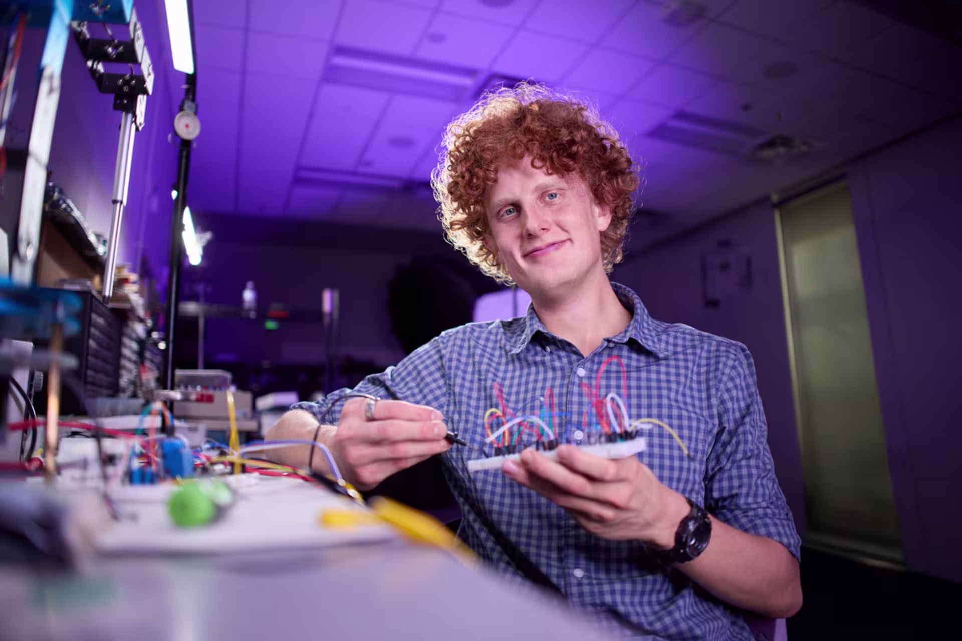 Electrical engineering student holding wires in a lab setting while smiling.