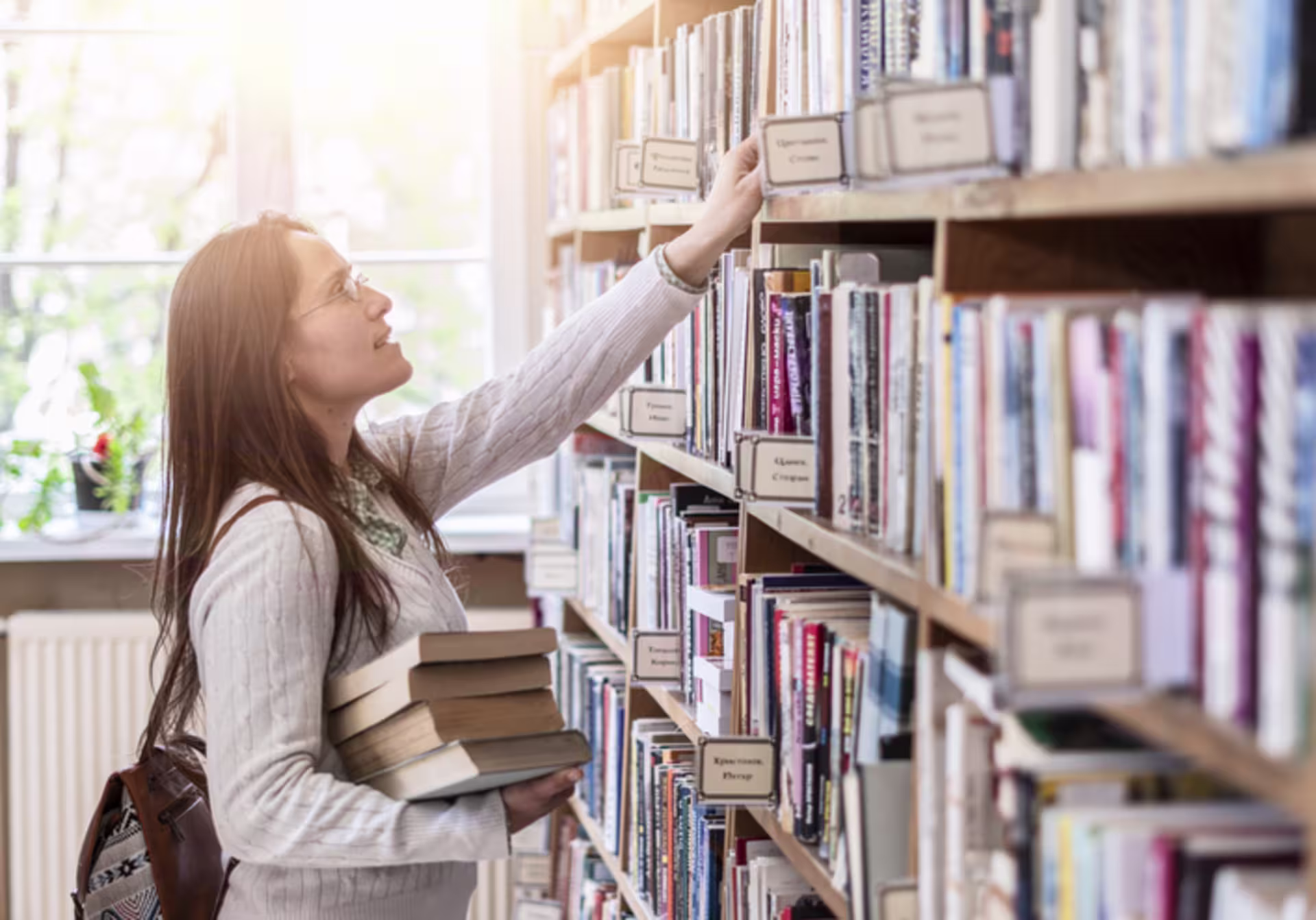 Student reaching for a book in a bright library, symbolizing the broad knowledge explored through general education courses.