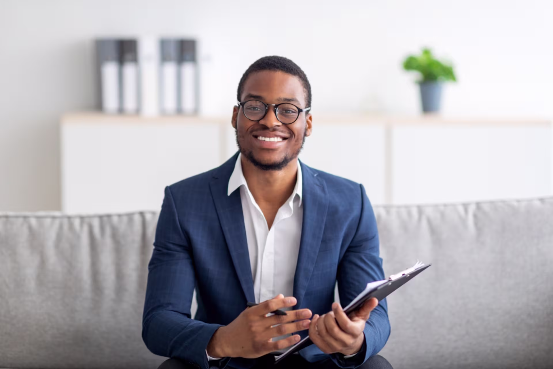Mental health counselor smiles in a blue suit on a couch.