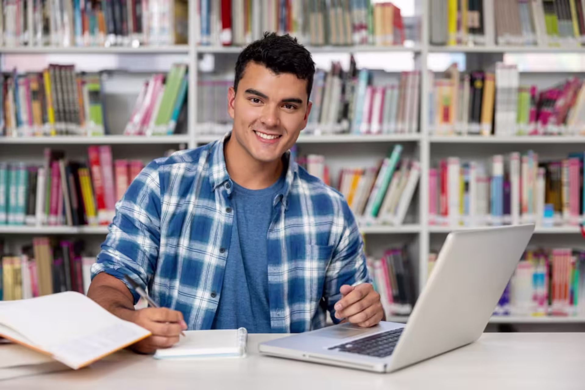 Male MEd Special Education student sitting in library with laptop and noteboo