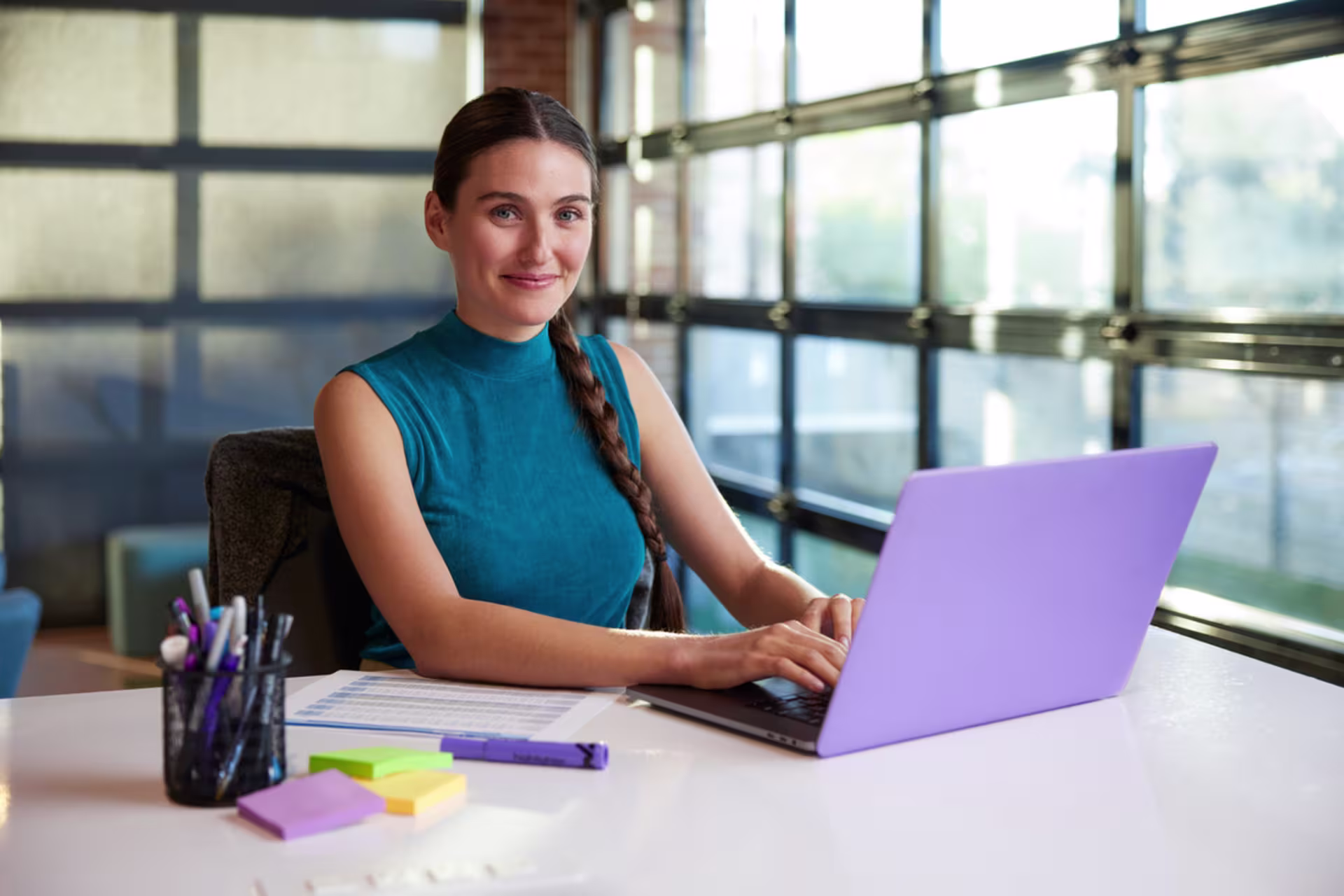 Female finance student in a blue tank top working on a purple laptop in an office setting.