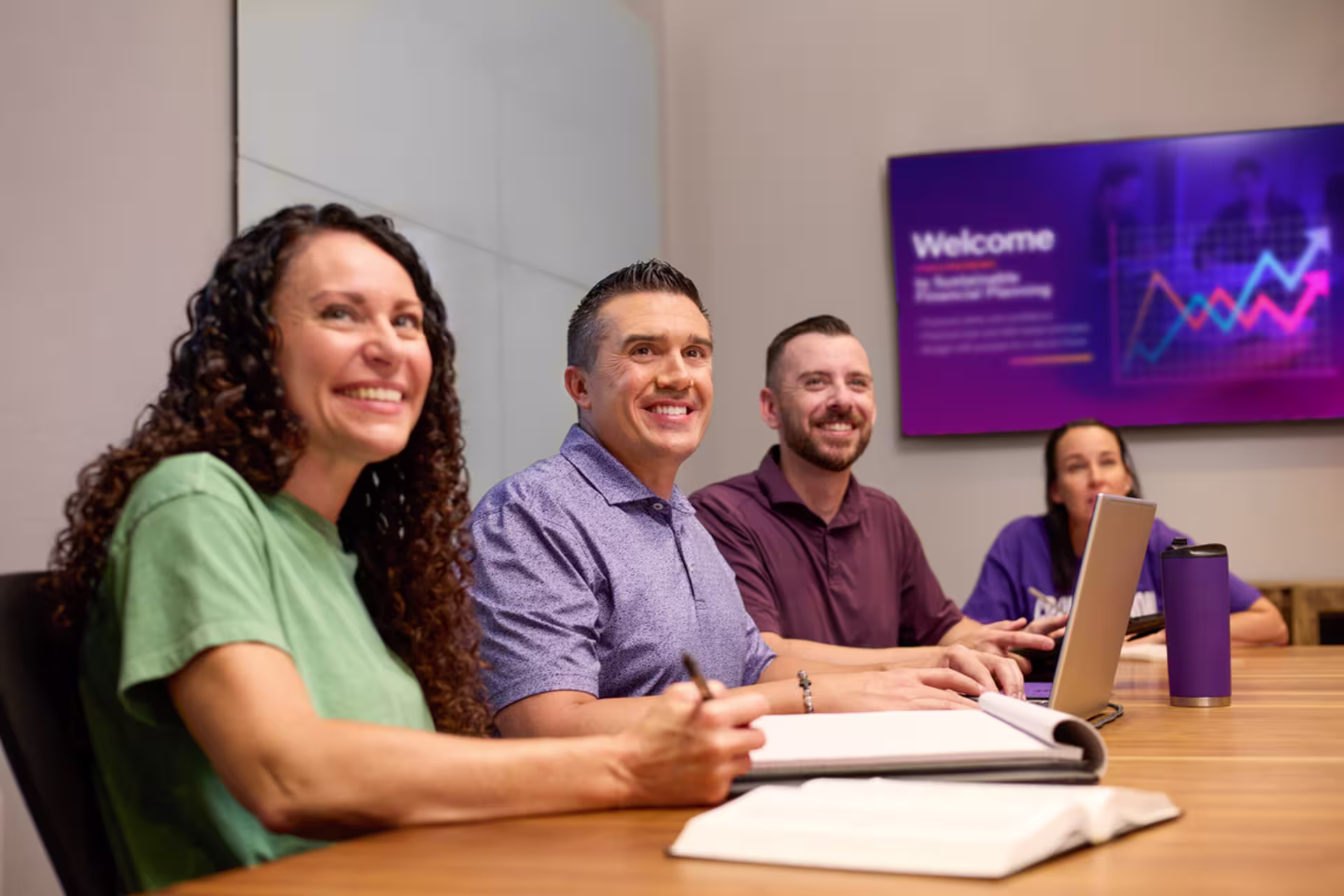 Male and female MBA students smile as they collaborate on a group project, seated at a table in a study room.