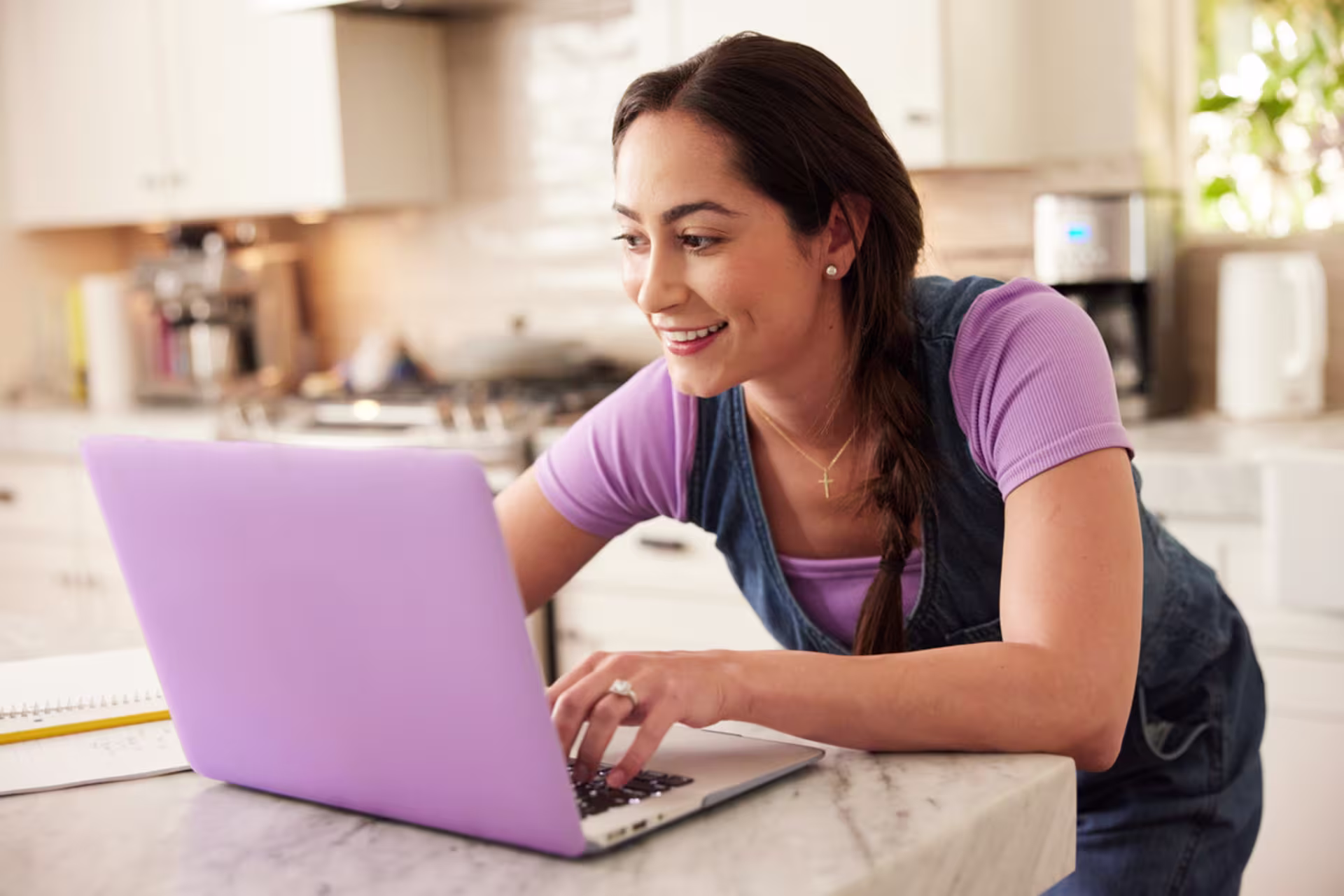 Online MS in OT Bridge student working on classwork on a laptop from home in a kitchen setting.
