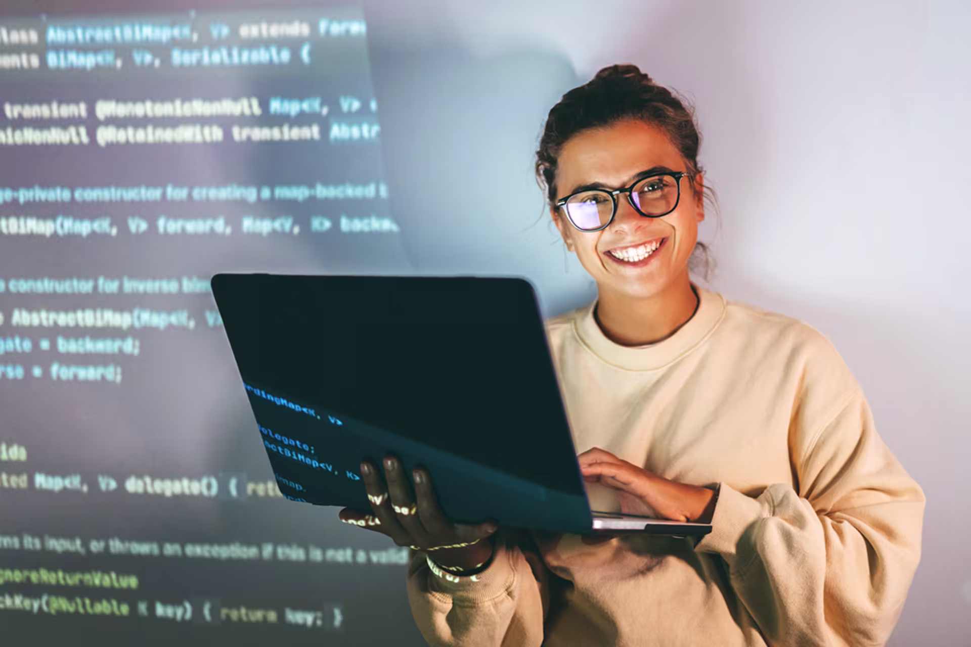 bachelor's-level technology student smiles holding laptop with code on screen behind her
