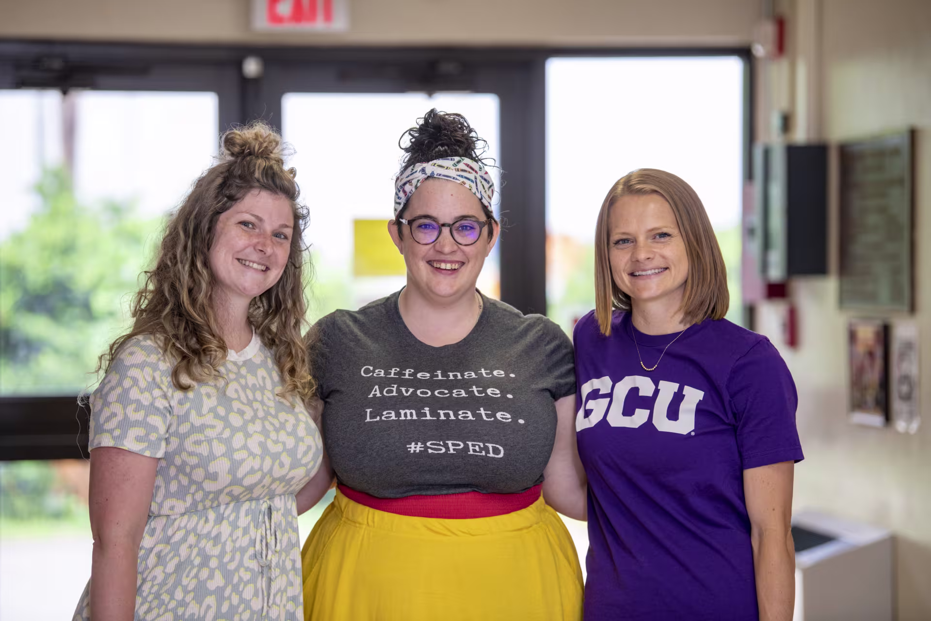 Three students smiling in hallway.