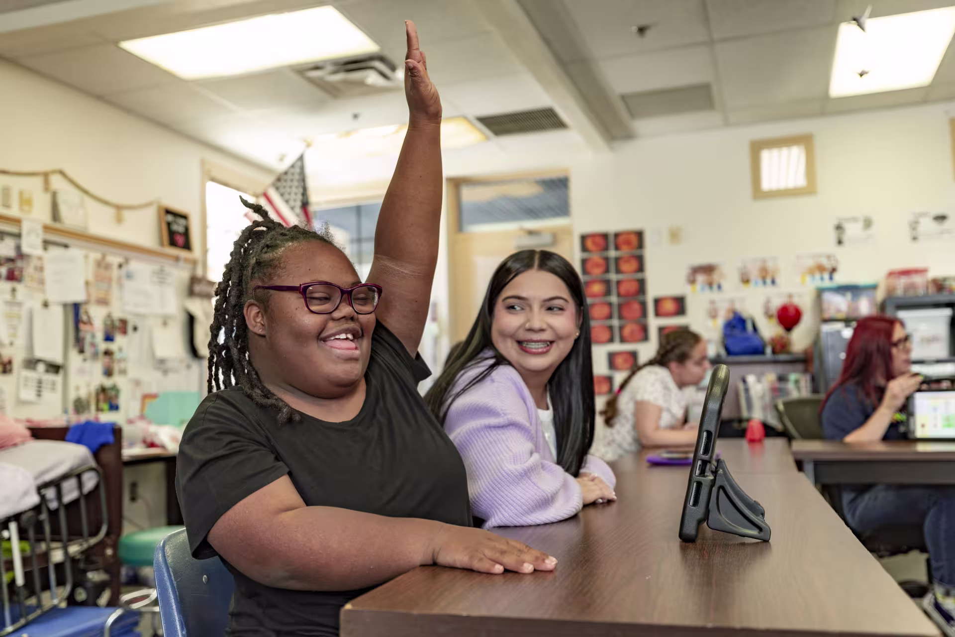 girl raising hand next to teacher in classroom