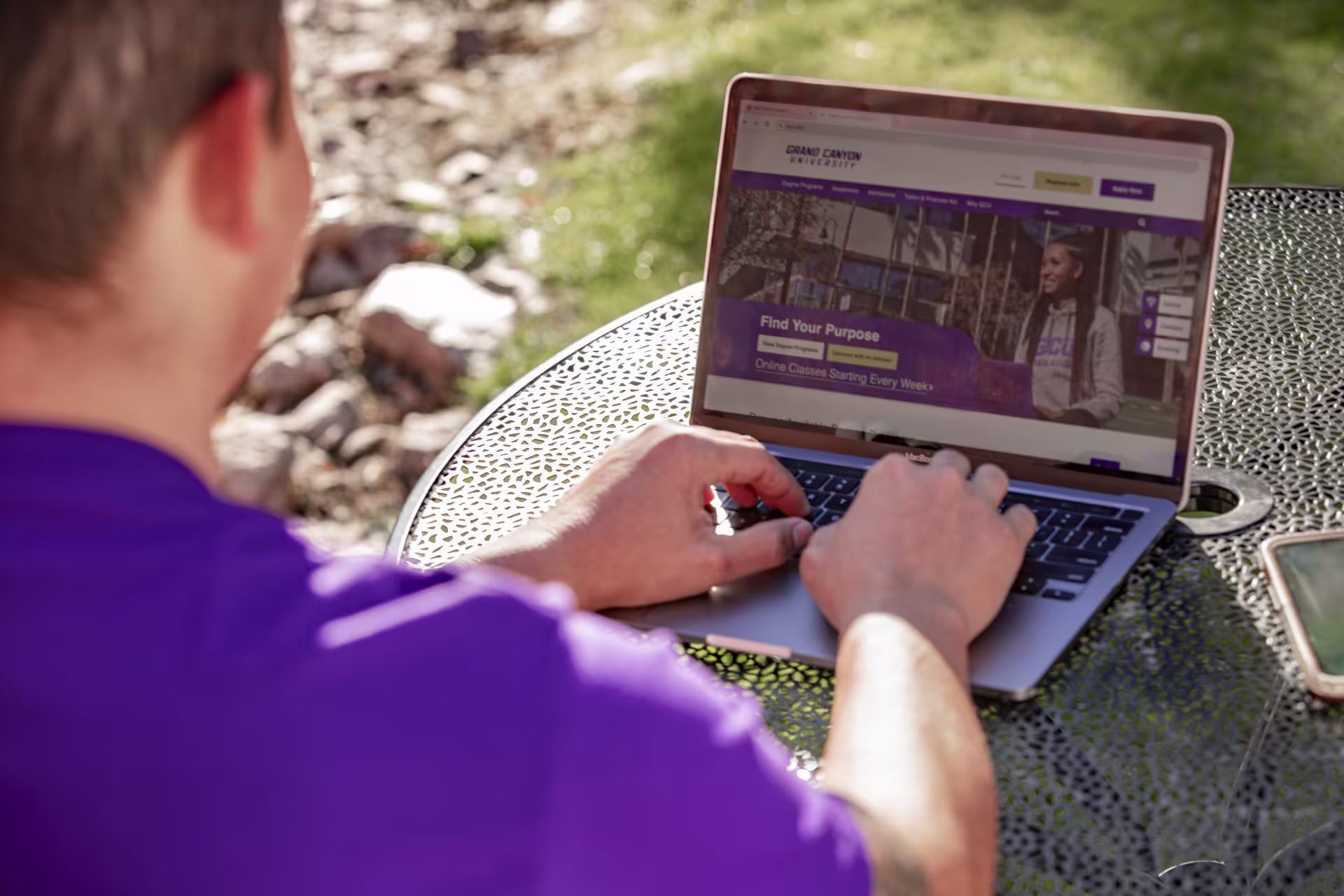 Man sitting outside using laptop to apply to GCU online