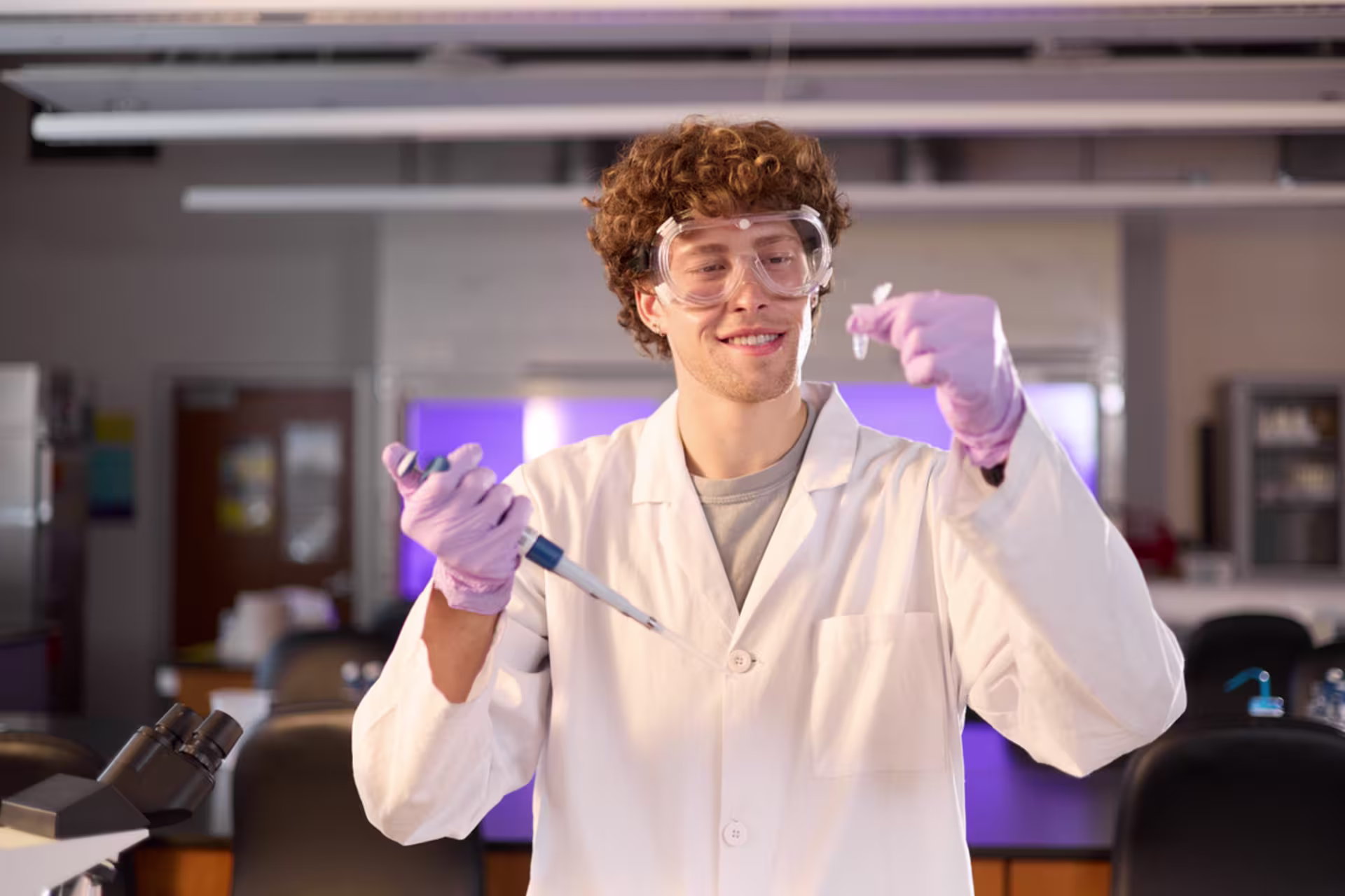 Medical lab sciences student in white coat and purple gloves working in a lab setting.