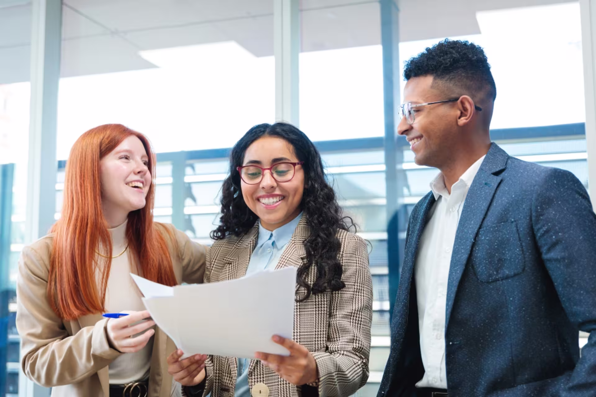 Three colleagues smiling and reviewing documents together in a bright modern office, demonstrating teamwork and leadership.