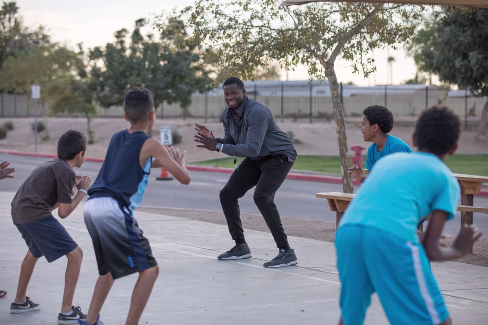 Male PE teacher coaching group of young male students on outdoor basketball court.