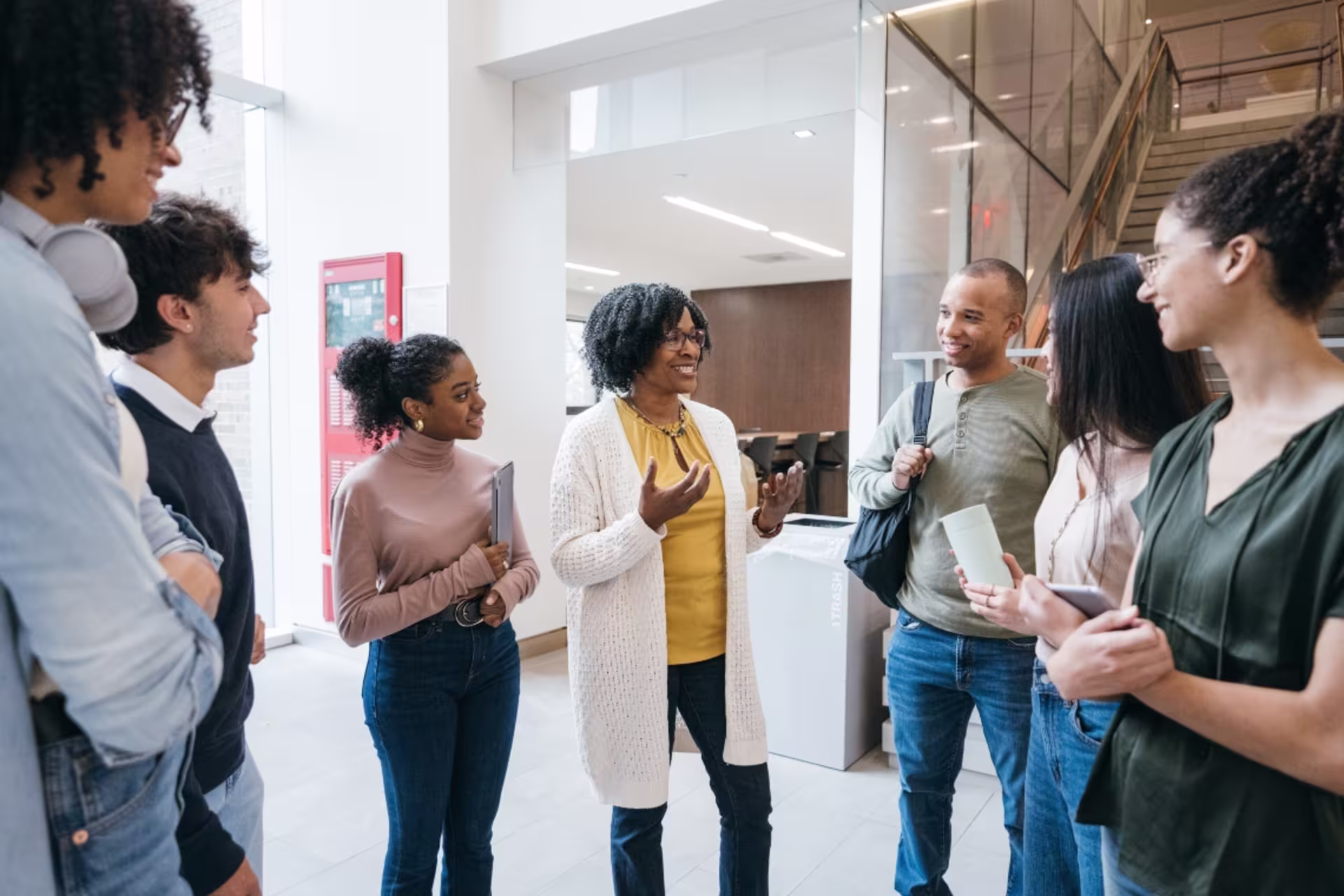 A student affairs professional speaks with a group of college students in a bright campus building.
