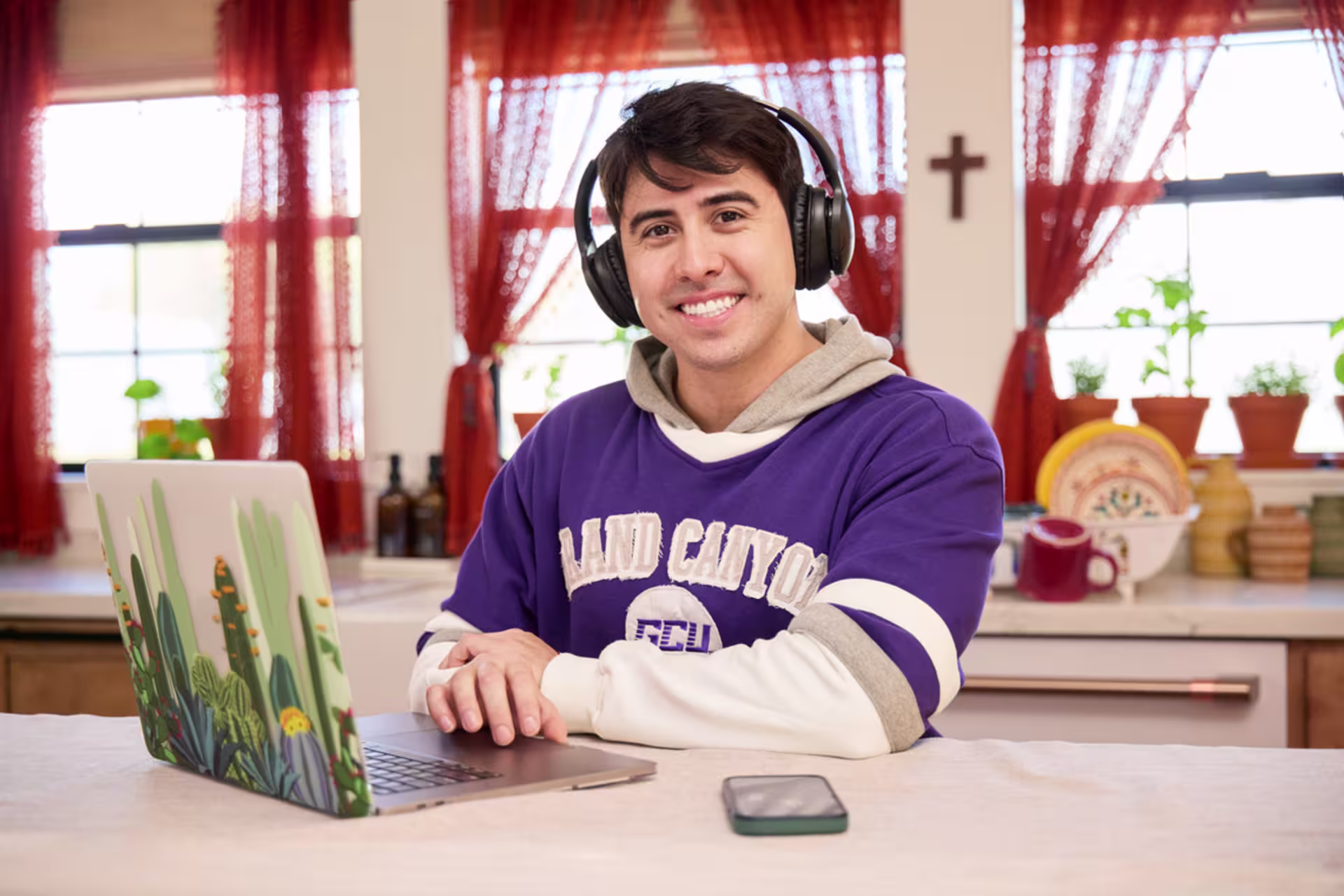Male online student in purple sports jersey and headphones smiling while sitting at a desk with a computer.