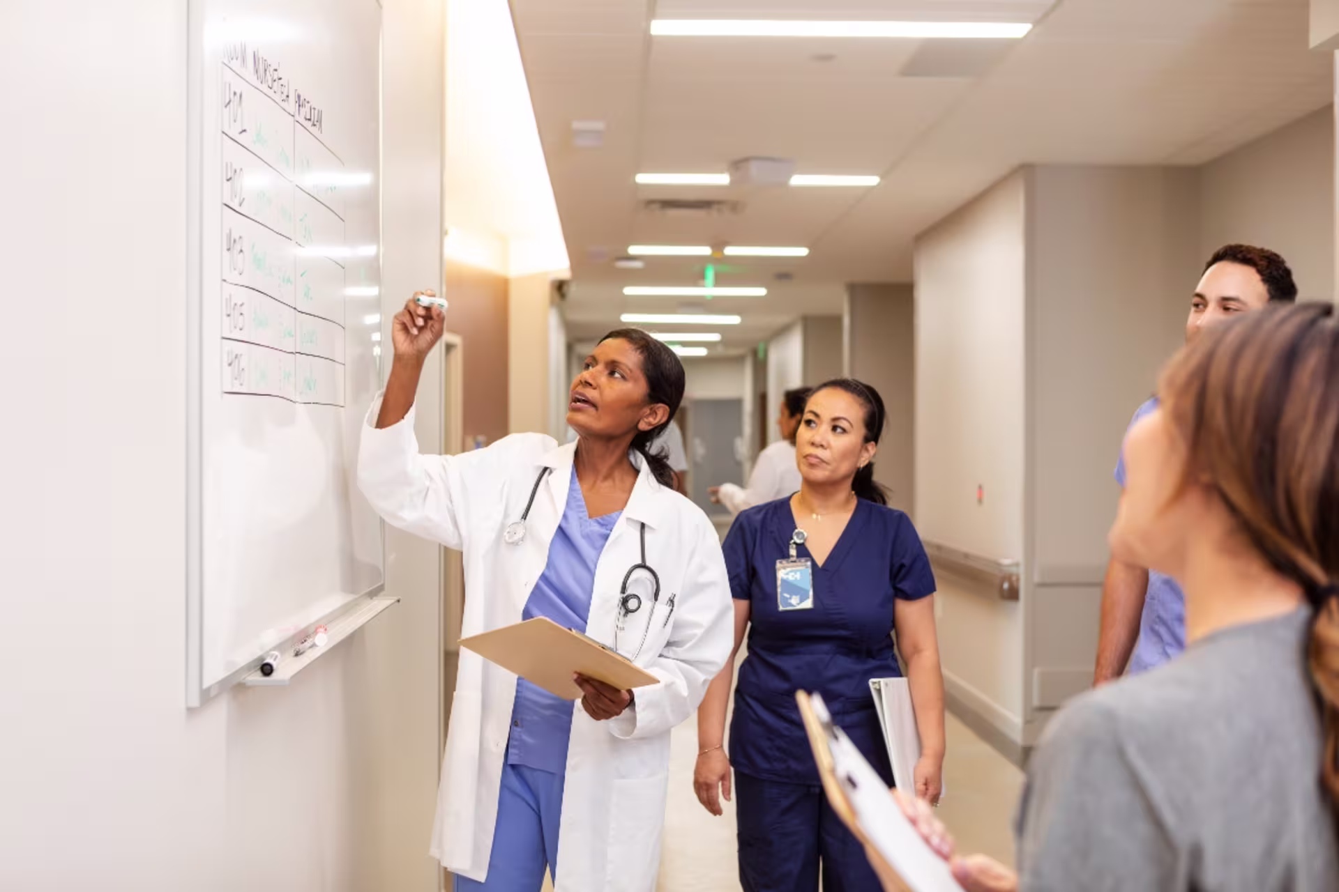 A group of nurses review patient information on a white board in a hospital.