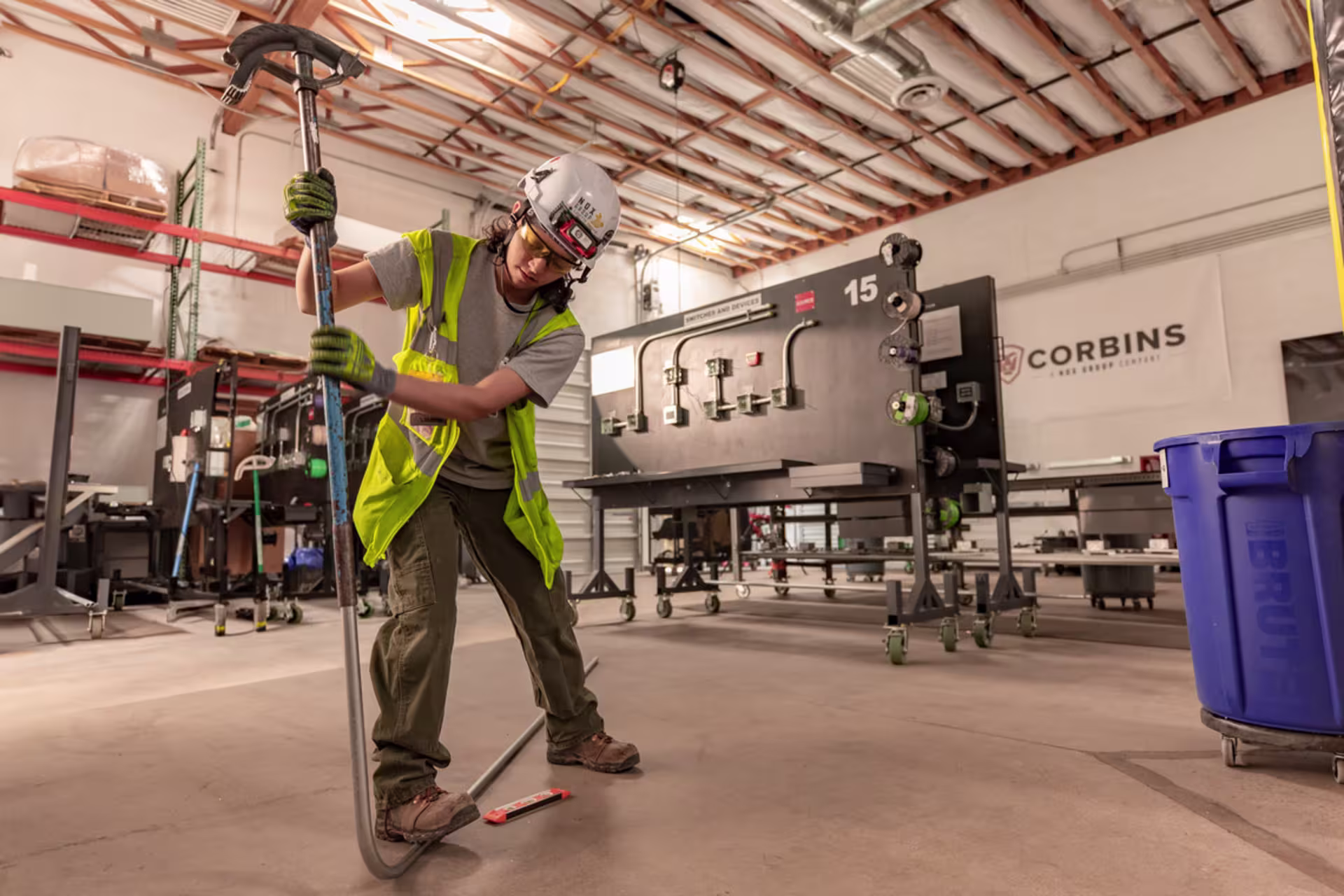 Facilities engineering student wearing safety gear and bending conduit in an industrial training lab.
