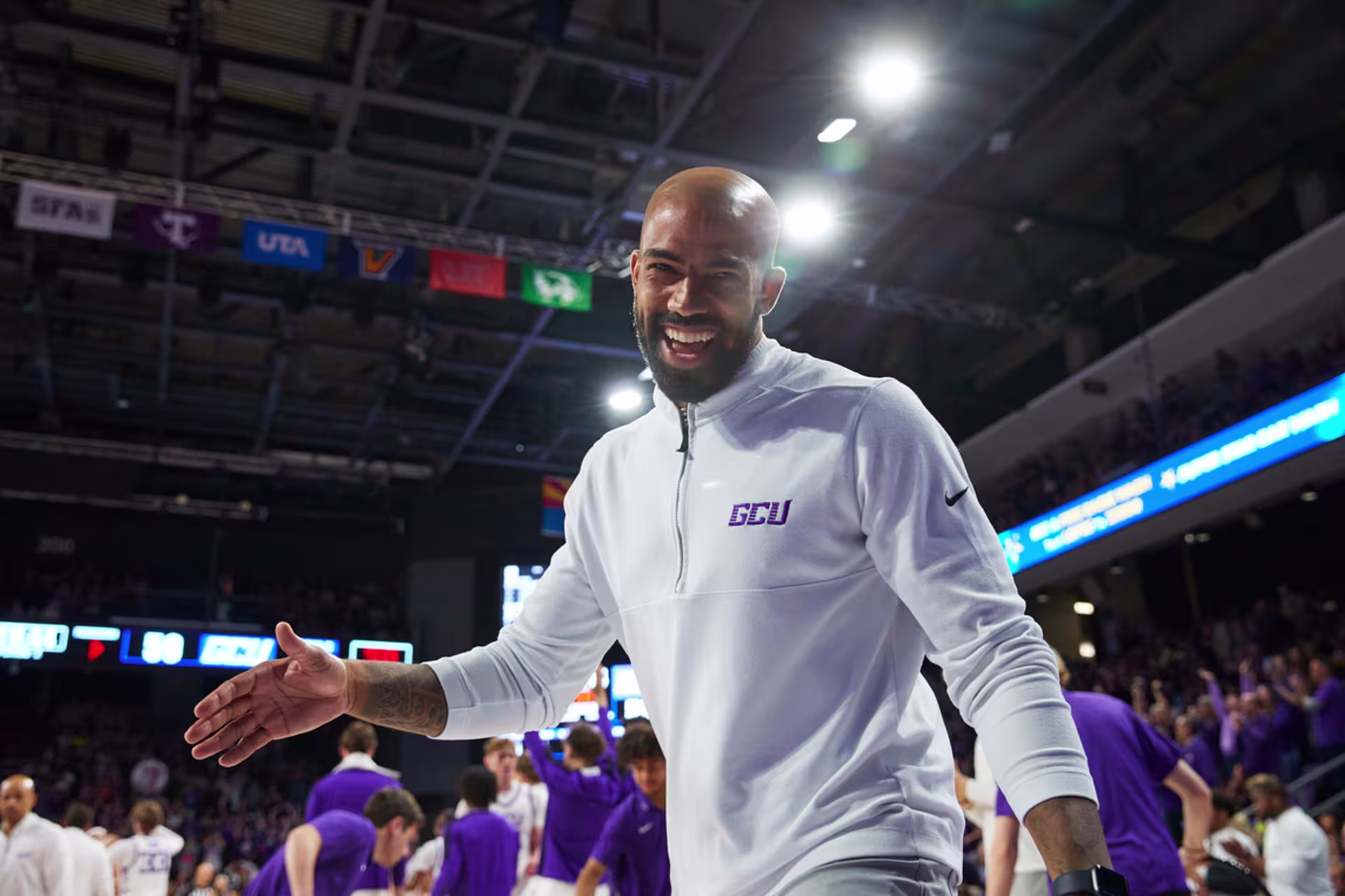 Male sport and performance psychology graduate walking on the sidelines of a basketball court, during a game, with players in the background.