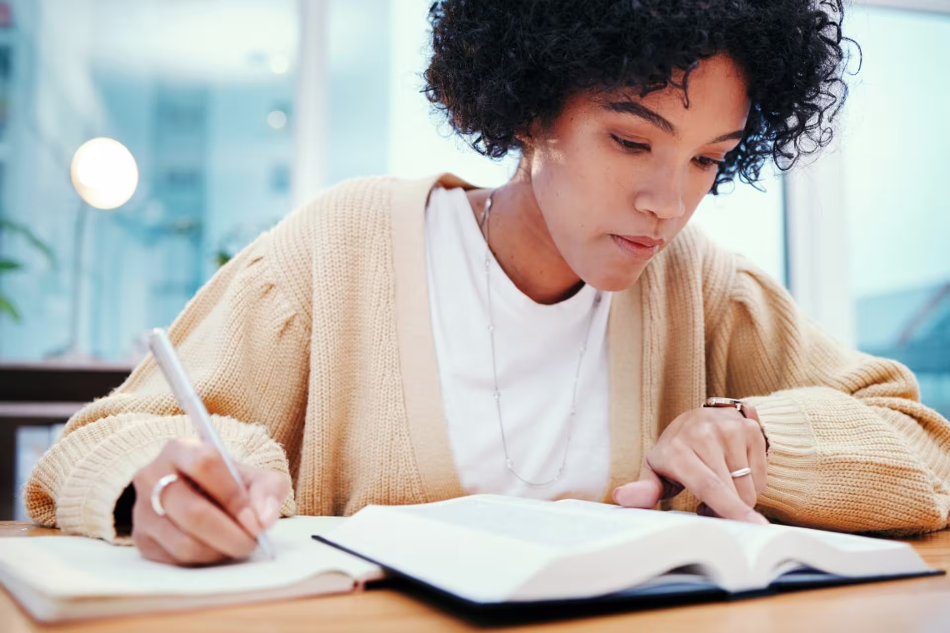 Old Testament studies student in a cream cardigan, taking notes as she reads the Bible.