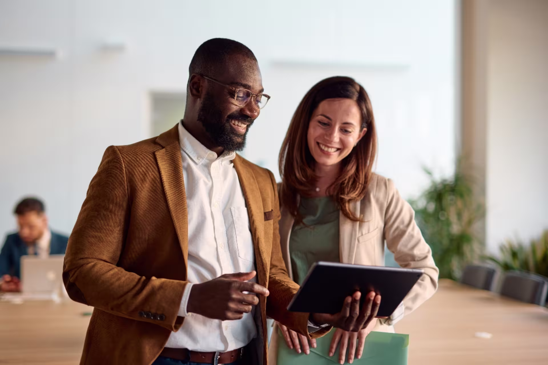 Two professionals reviewing information on a digital tablet during a business meeting in a modern office setting.