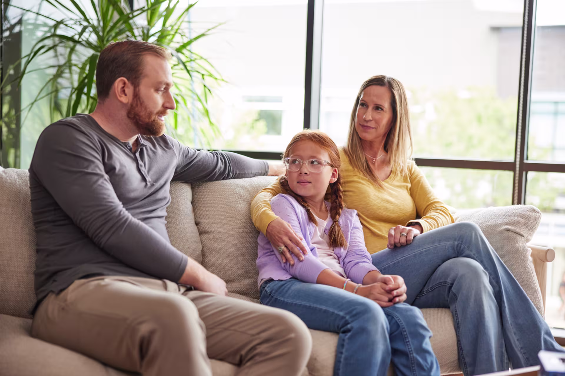 Mother, father and daughter sitting together on a couch having a session in a counselor's office.