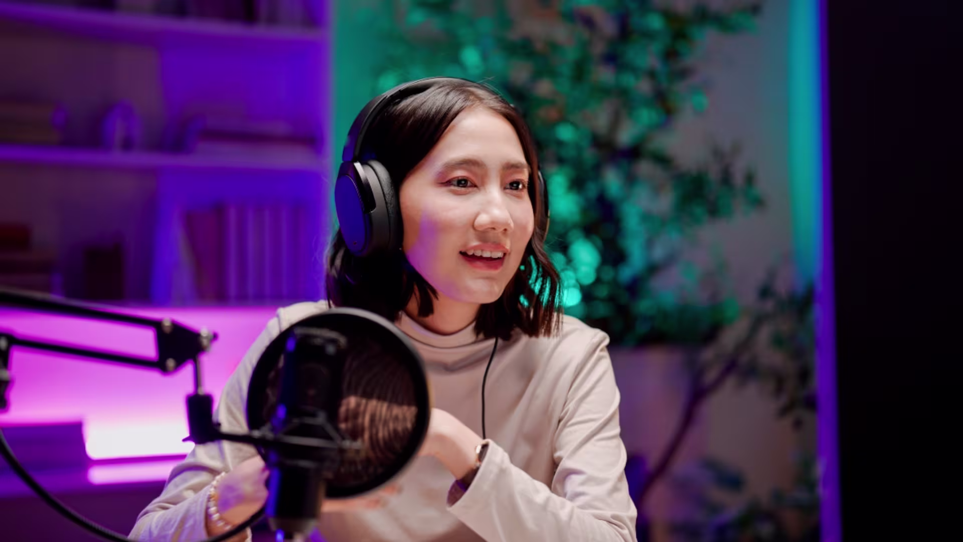 Young Asian woman wearing headphones and talking into a microphone during a podcast session.