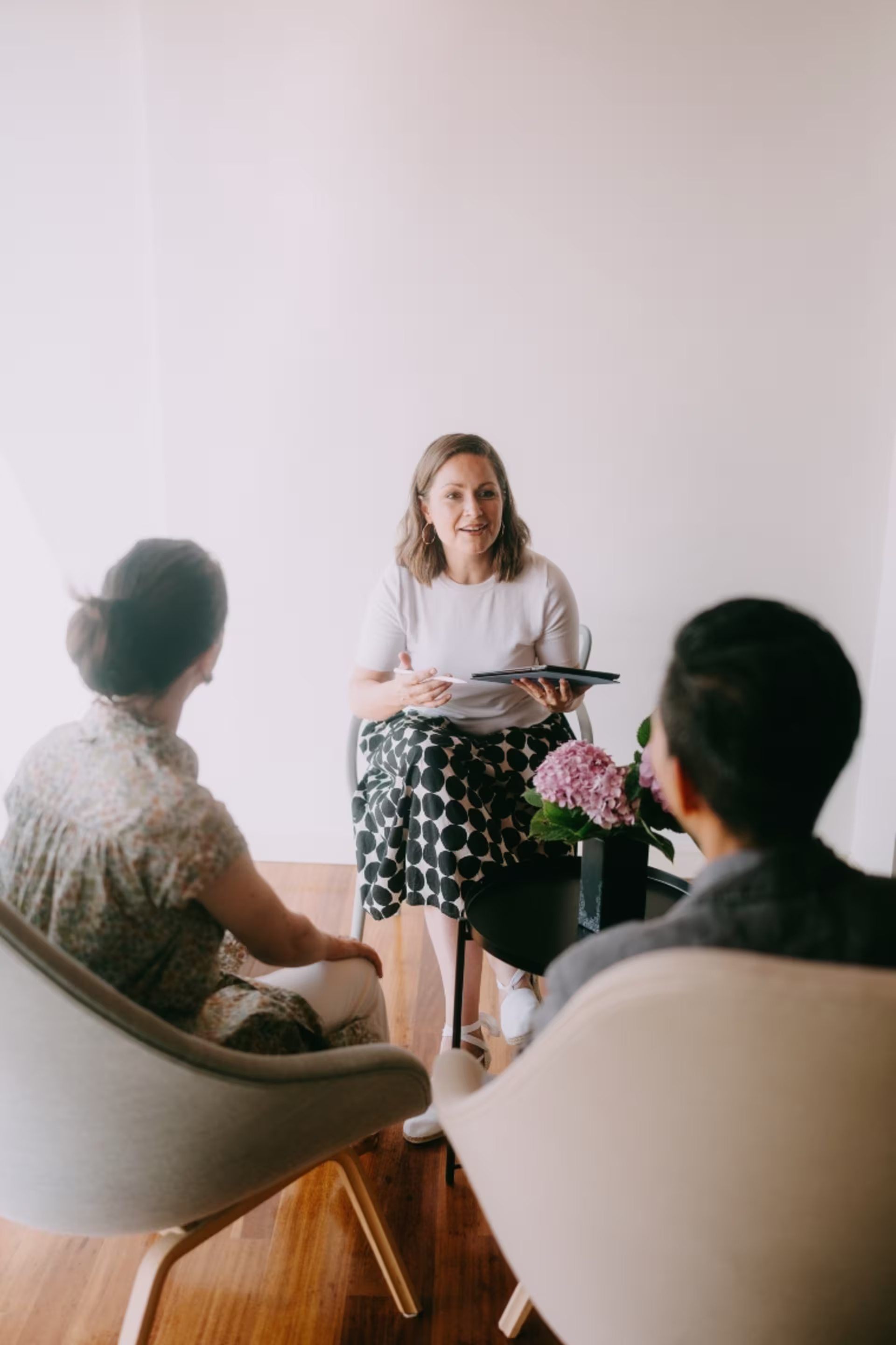 Counselor meeting with two adults in a small office, holding a tablet and speaking while they listen.