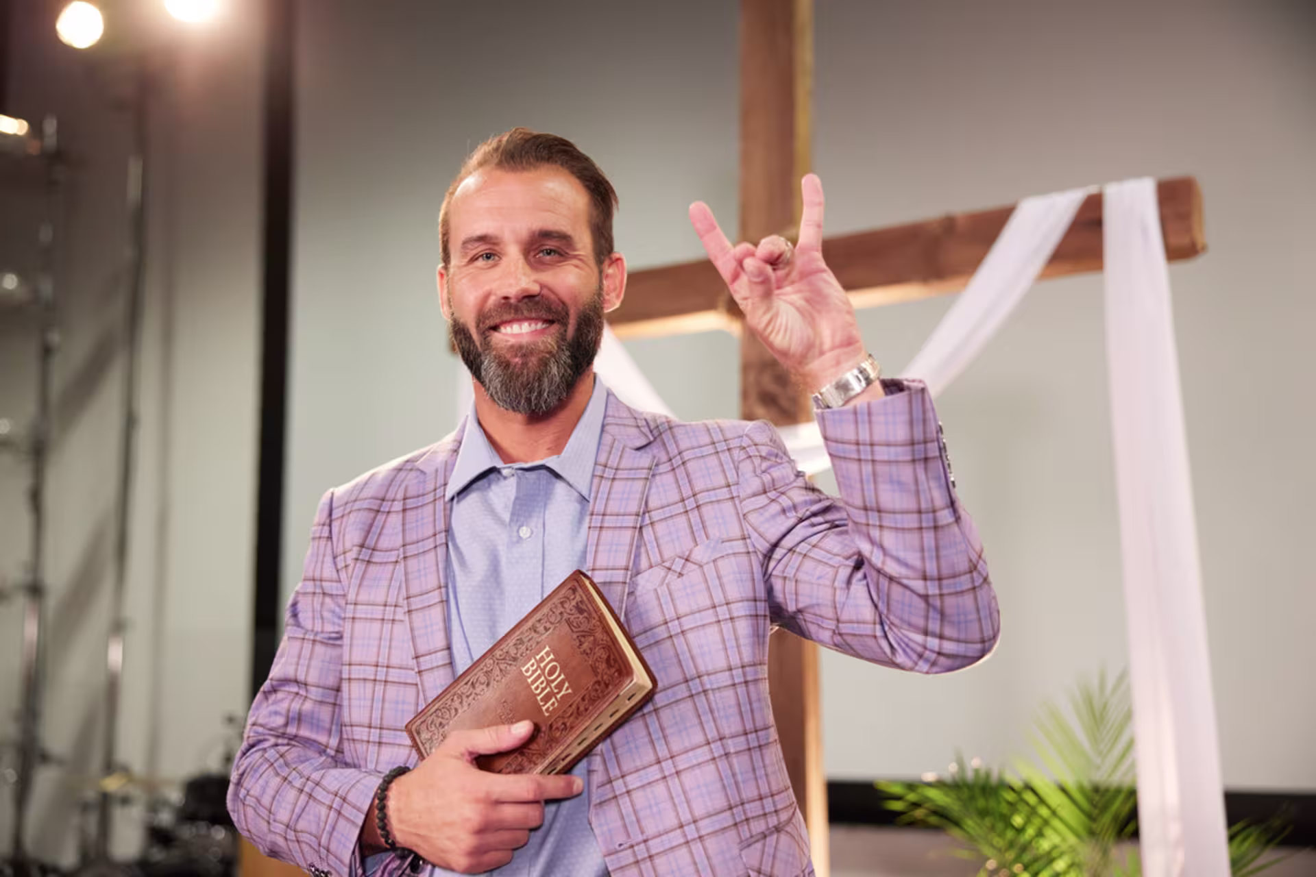 Minister smiling in a church setting while throwing lopes and holding a bible.