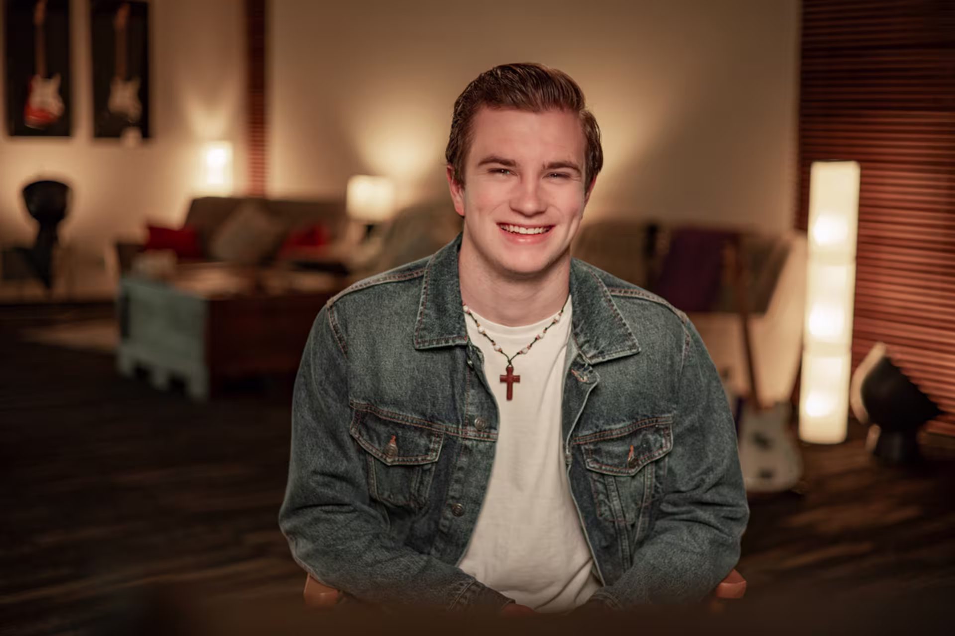 Person wearing a cross necklace seated in a warm, worship-inspired room, reflecting themes of theology and ministry.