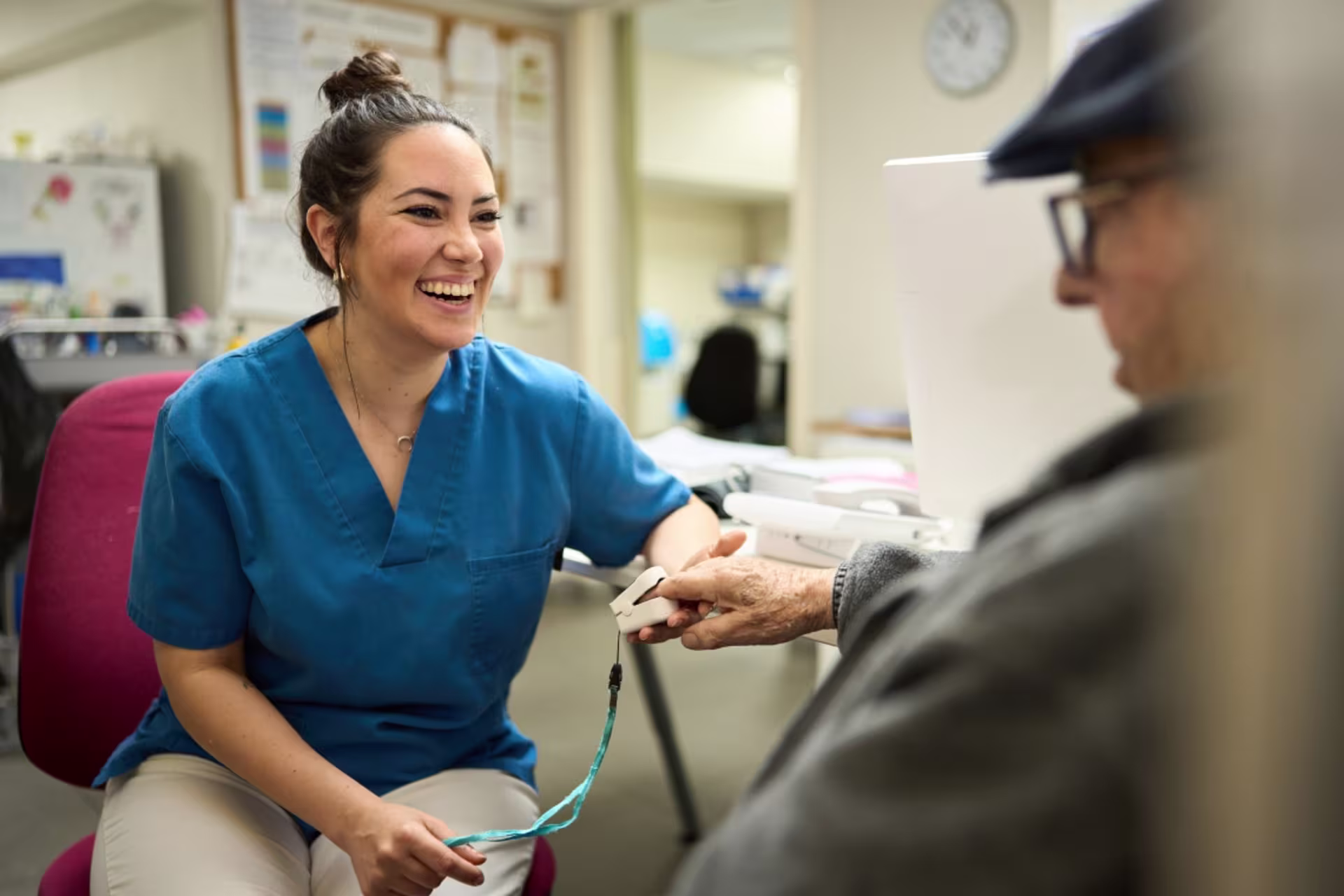 A female nurse sits and smiles while taking the vitals of a patient in a health clinic setting.