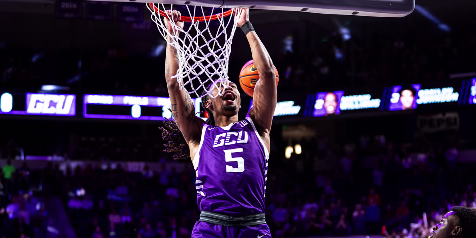 Shot from a GCU men’s basketball vs. New Mexico game of player hanging from rim after making a basket.