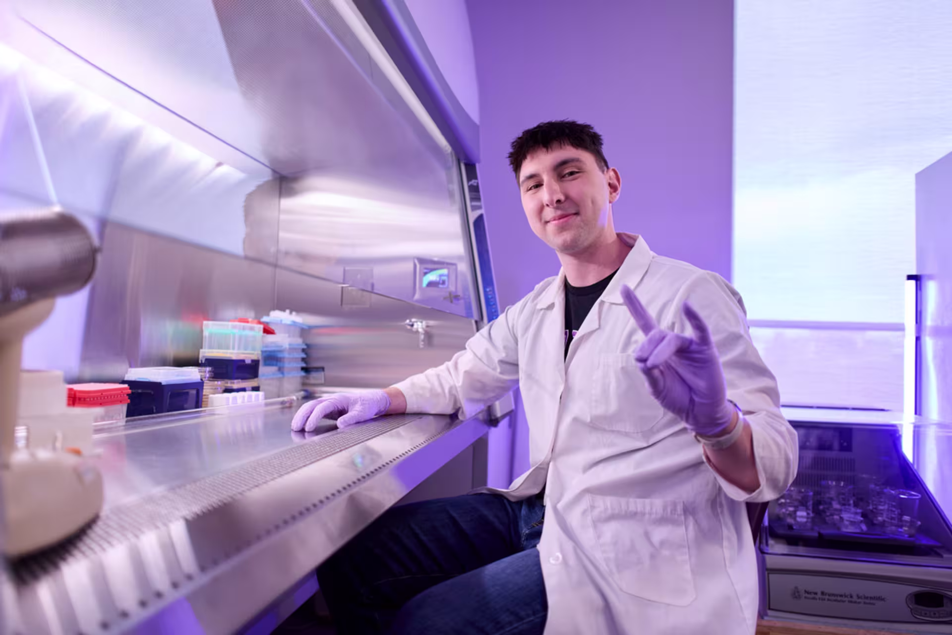 A pre‑med biology student works in a laboratory hood with samples and lab equipment.